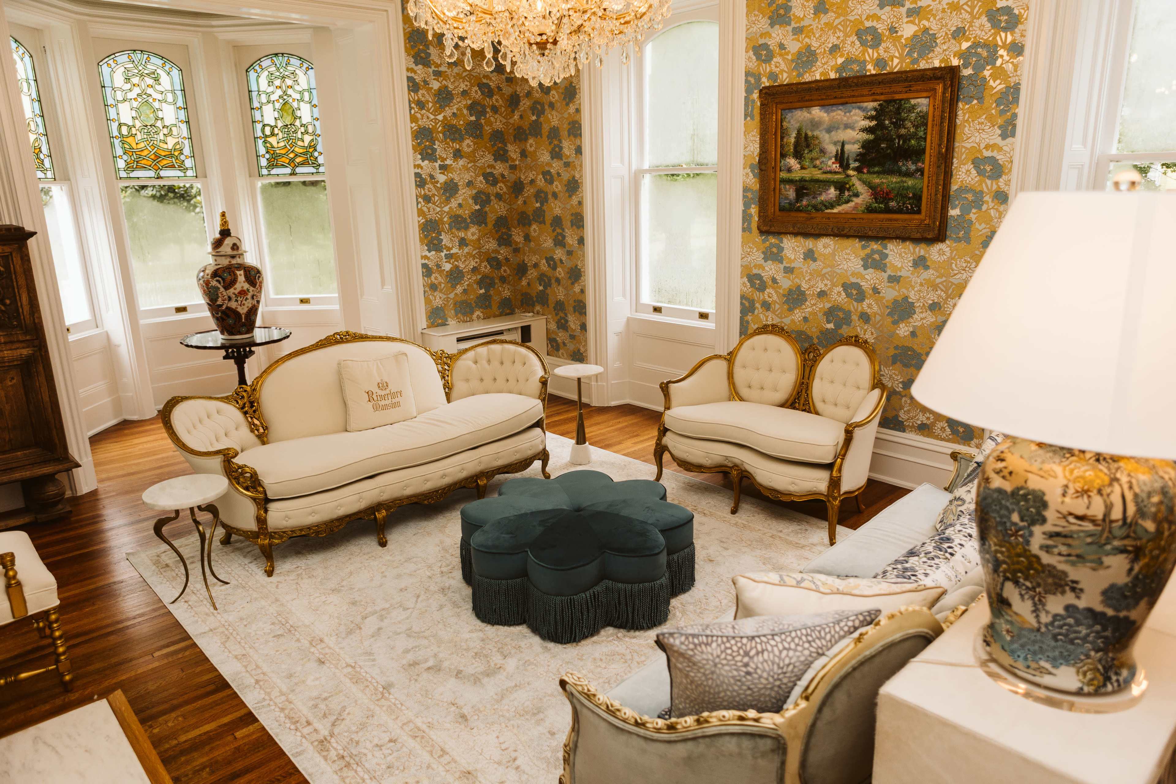 The image shows an elegantly decorated living room with vintage furniture, a chandelier, and patterned wallpaper.