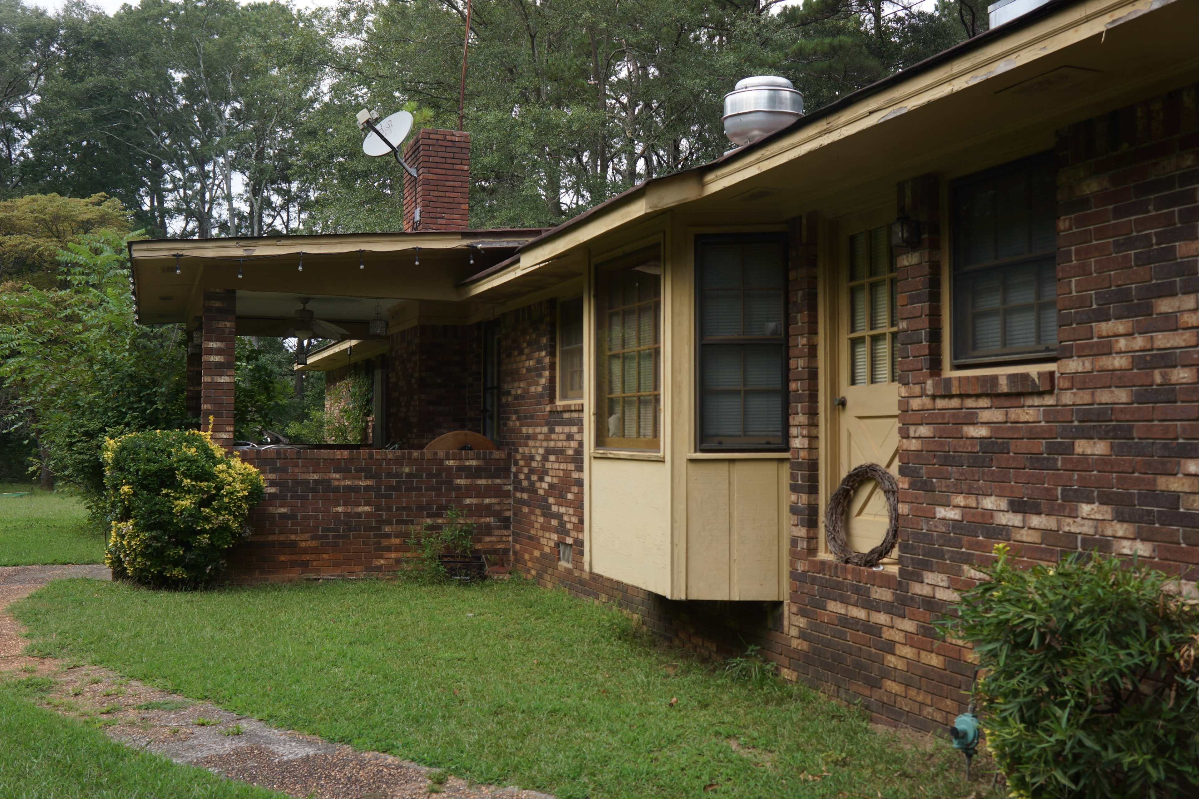 The image shows a brick house with a front porch, a satellite dish, and a well-maintained yard.