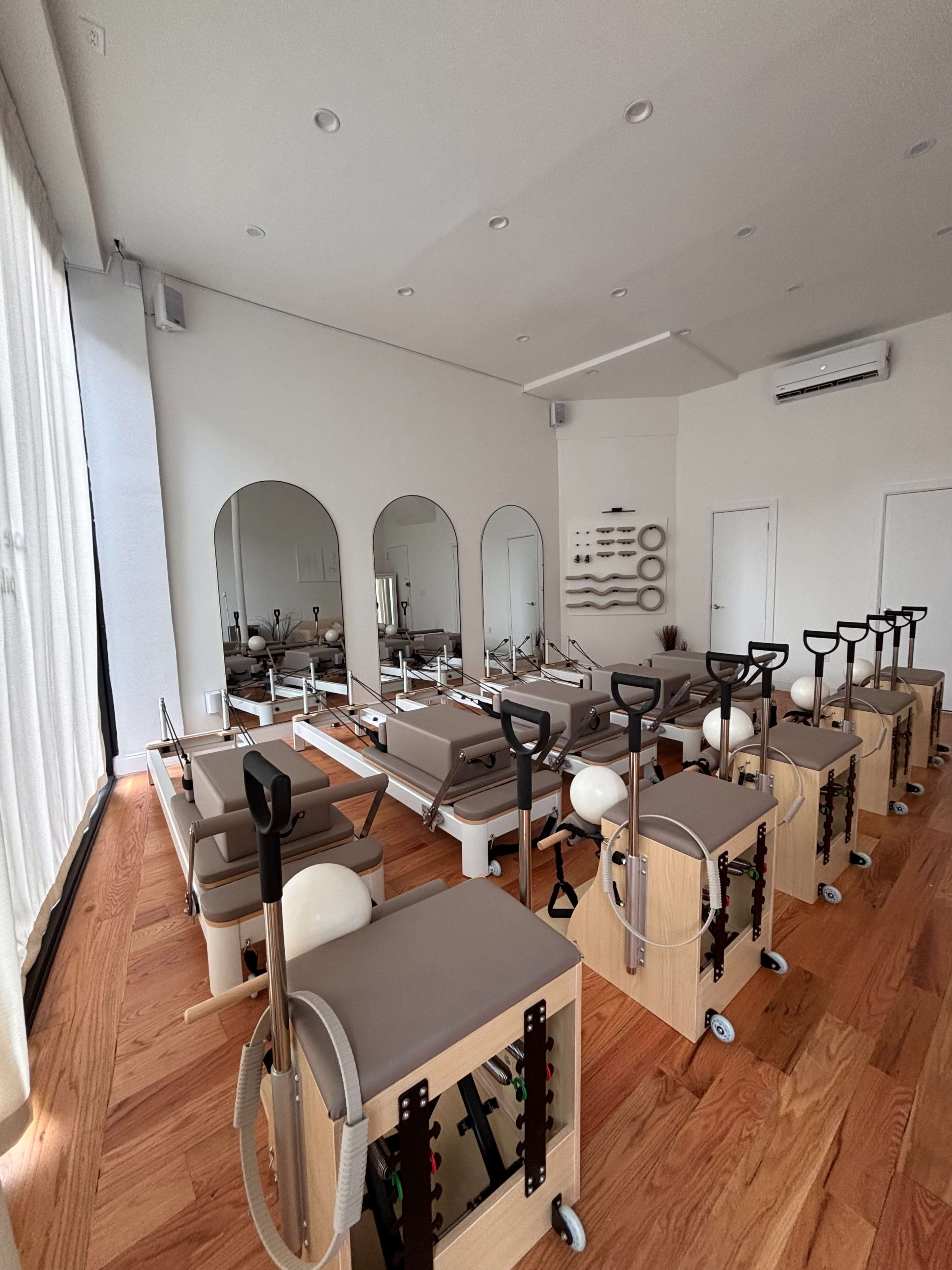 The image shows a well-organized Pilates studio with multiple reformer machines arranged in rows and large mirrors along the wall.