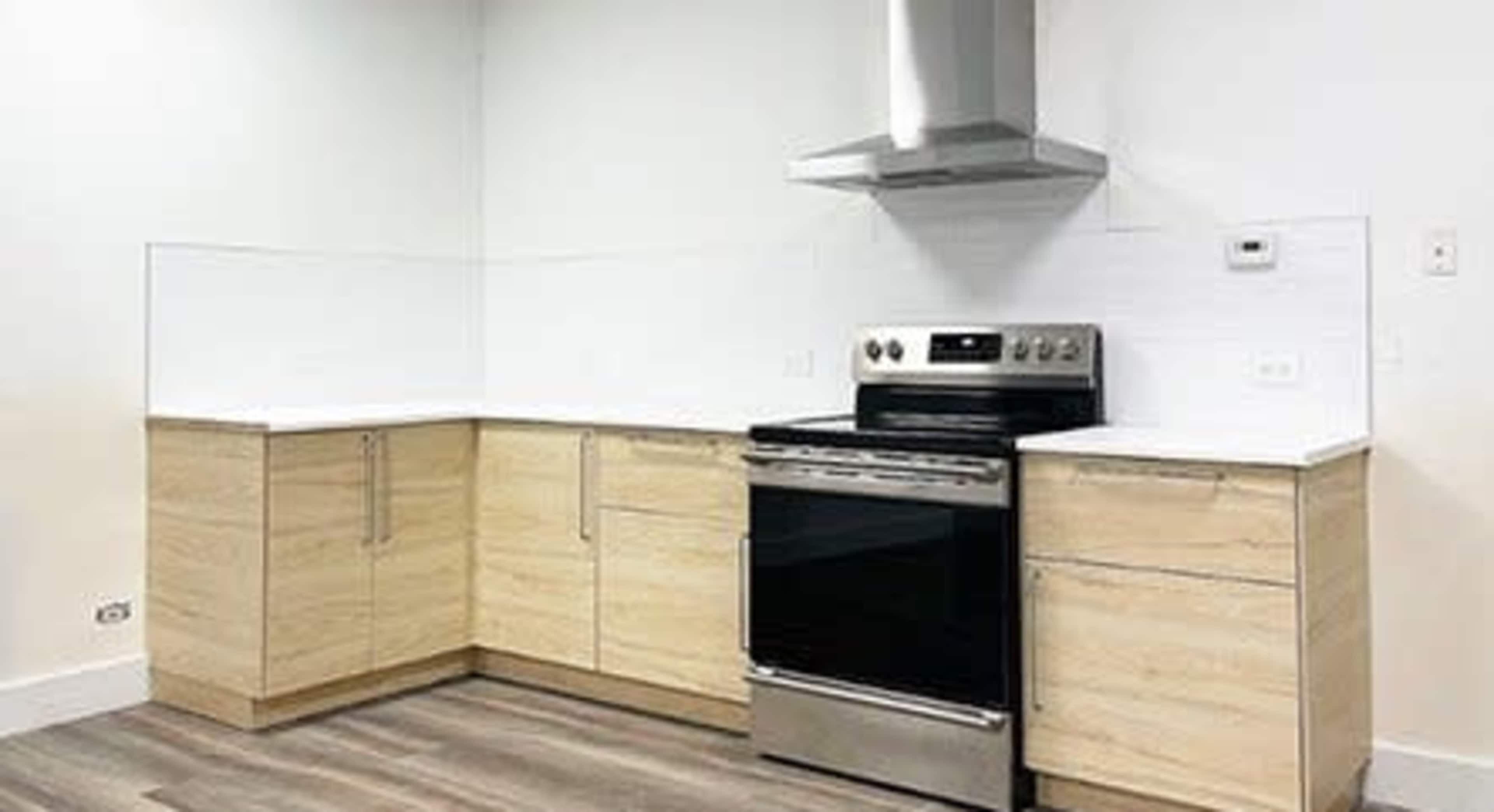 The image depicts a modern kitchen featuring light wood cabinets, stainless steel appliances, and a white backsplash.