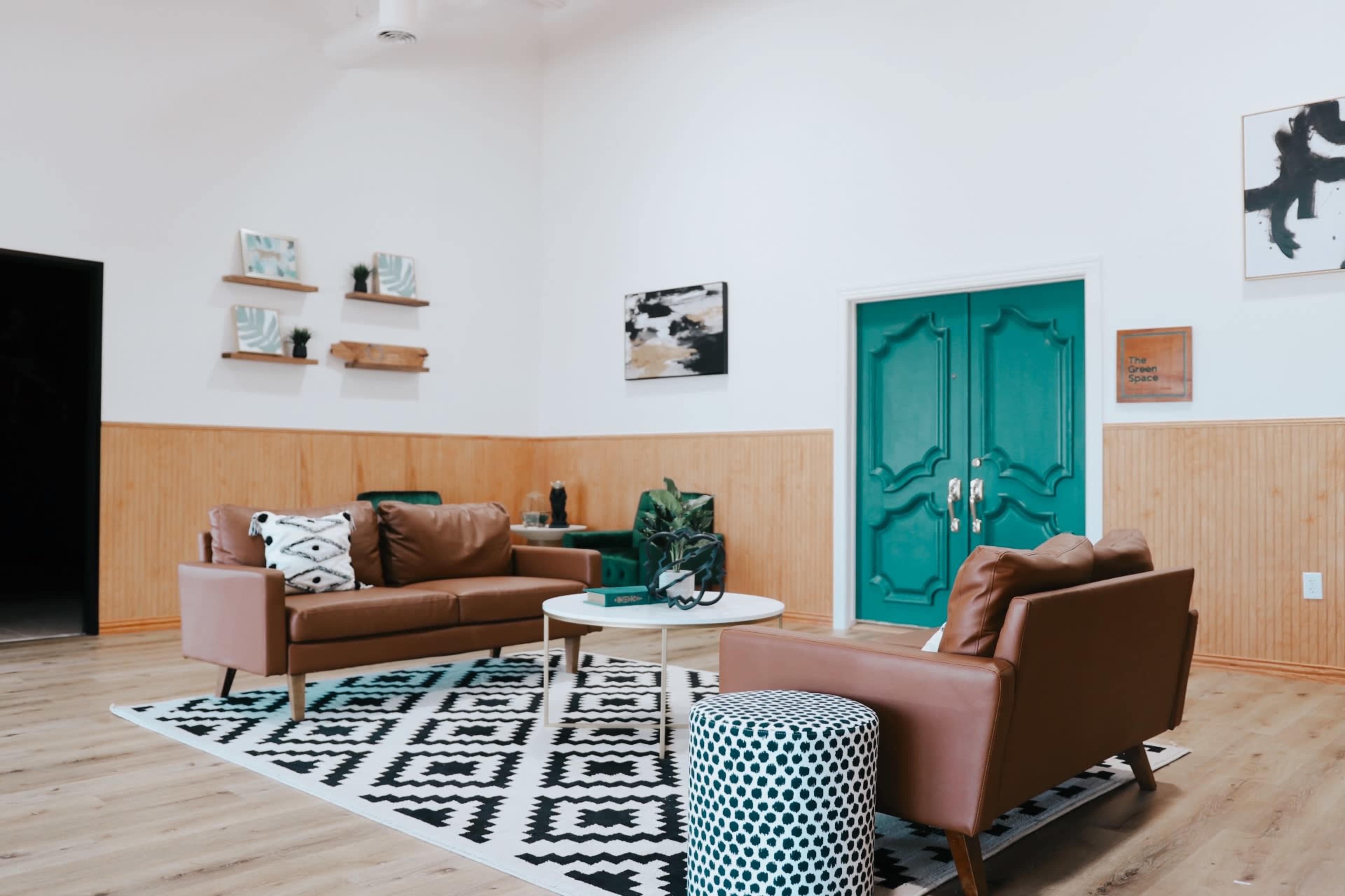 A modern living room features brown leather sofas, a round coffee table, and a patterned rug against a backdrop of white walls and teal doors.