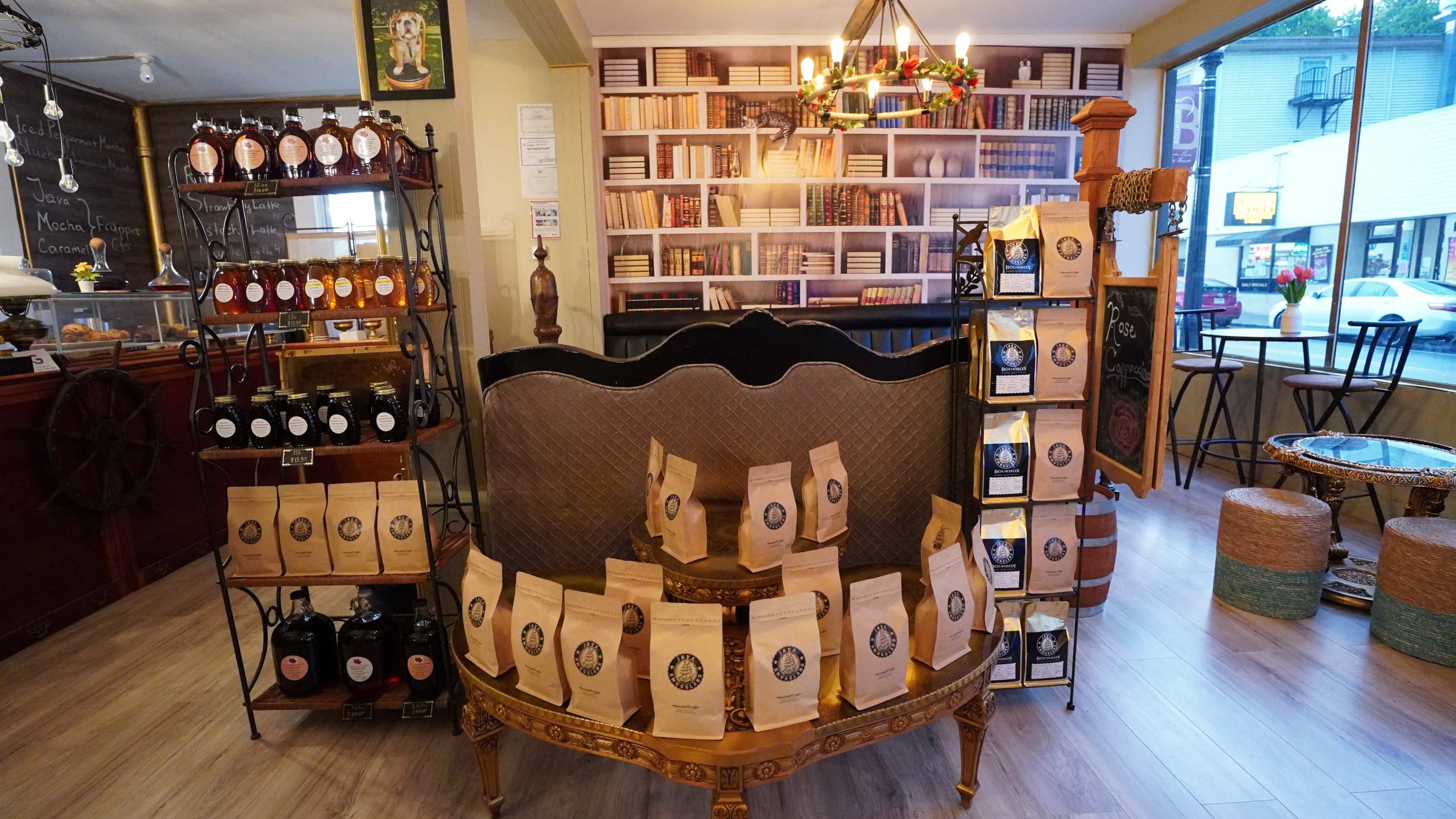 A cozy shop interior with shelves filled with books, various bottles on display, and bags of products arranged around a central decorative table.
