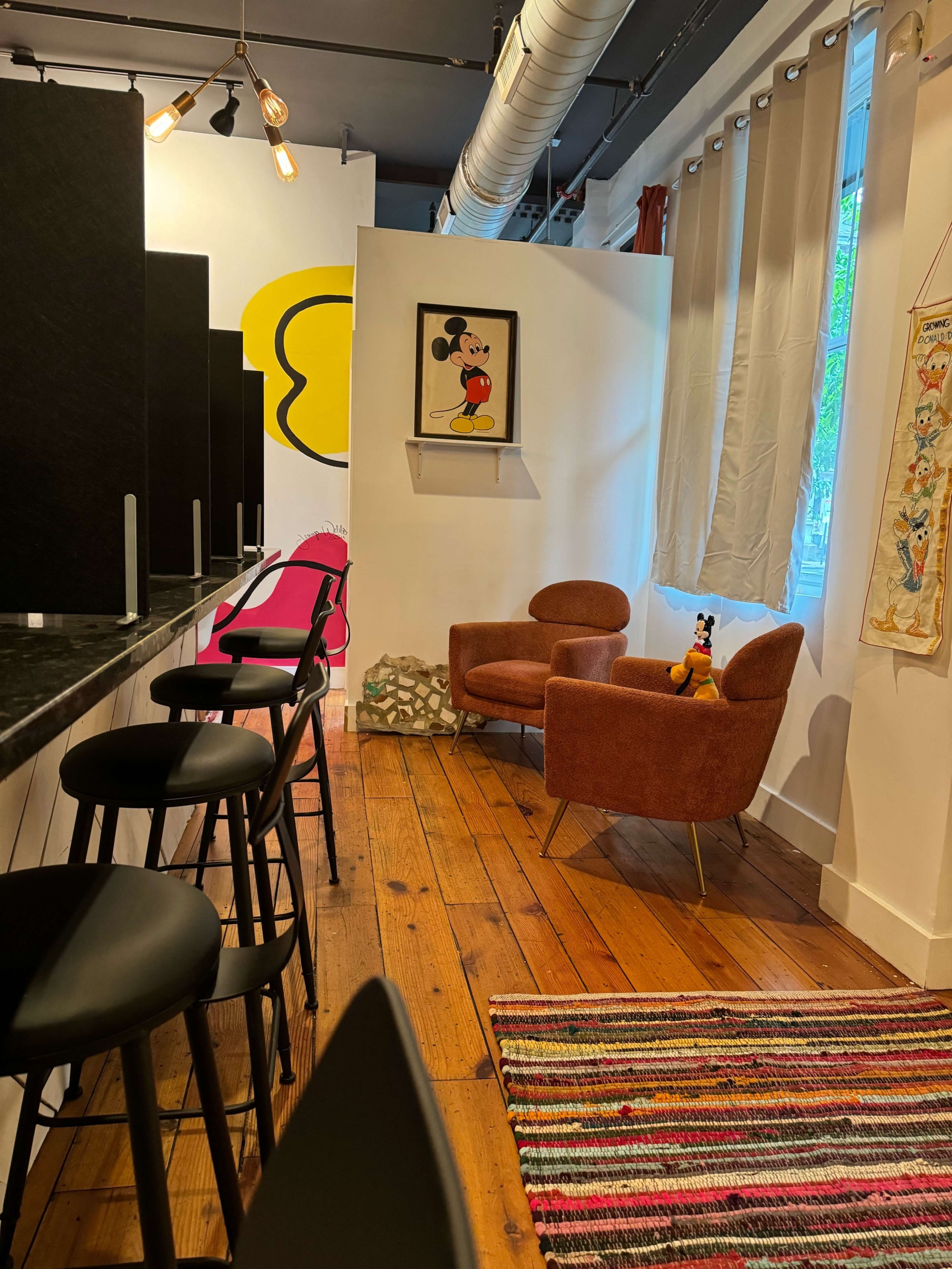 A cozy indoor space featuring a pair of orange armchairs, a colorful rug, and a wall adorned with a framed cartoon artwork of a character.