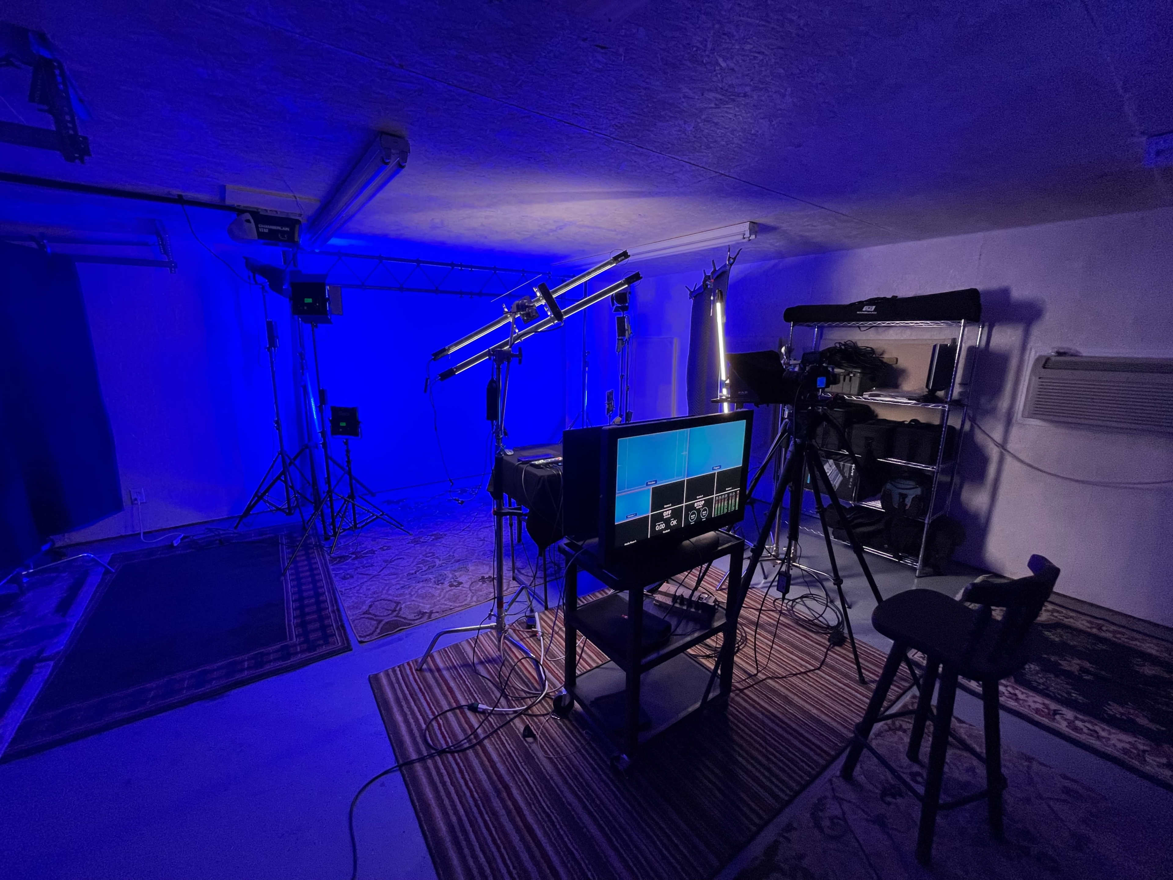 A dimly lit studio setup with blue lighting, featuring cameras, a monitor, and various equipment arranged on a table.