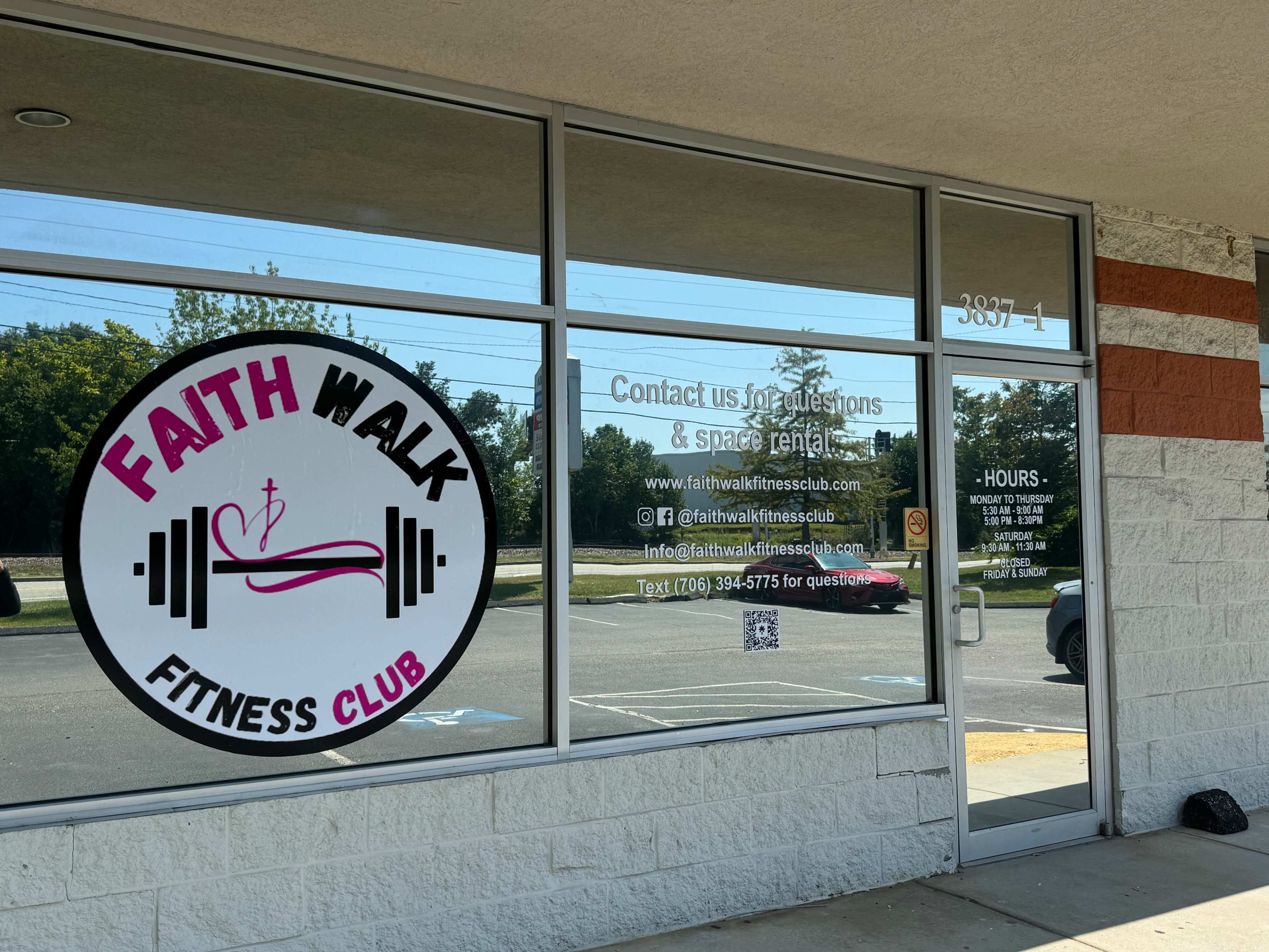 The storefront of Faith Walk Fitness Club, featuring large windows with a logo and contact information.