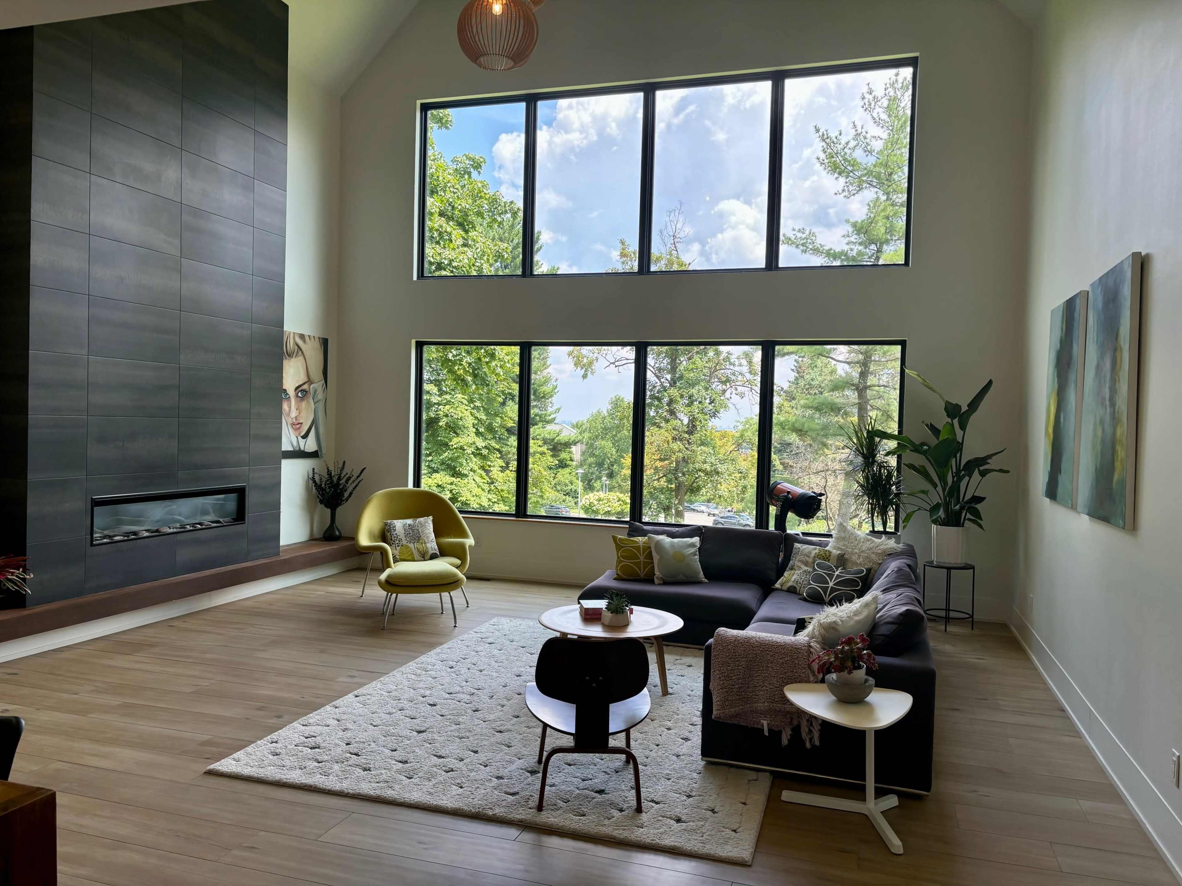 A modern living room with large windows, a sectional sofa, a yellow accent chair, and a coffee table on a light rug.