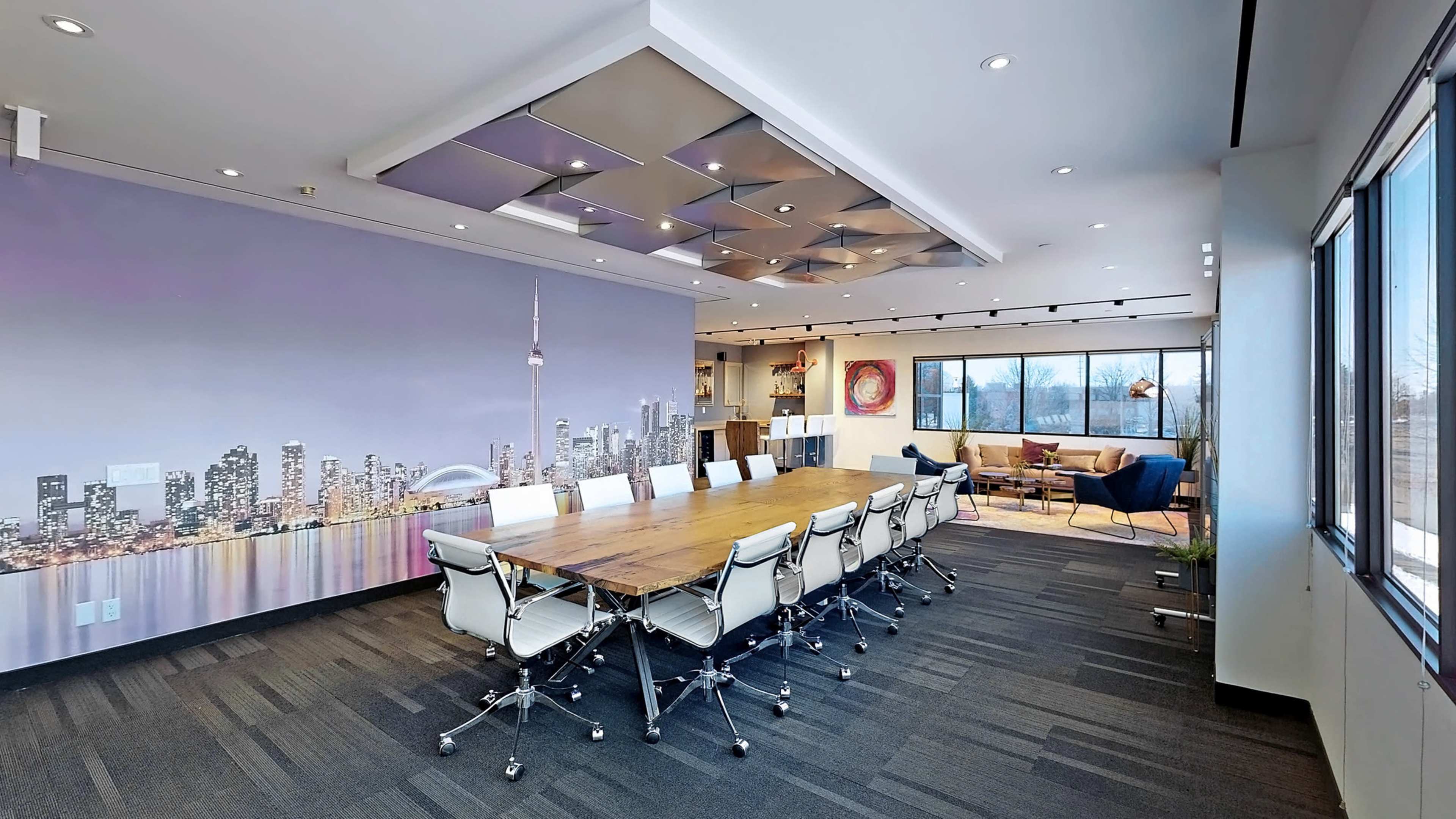 The image shows a modern conference room with a long wooden table and white chairs, featuring a city skyline mural on one wall and a lounge area with a sofa in the background.