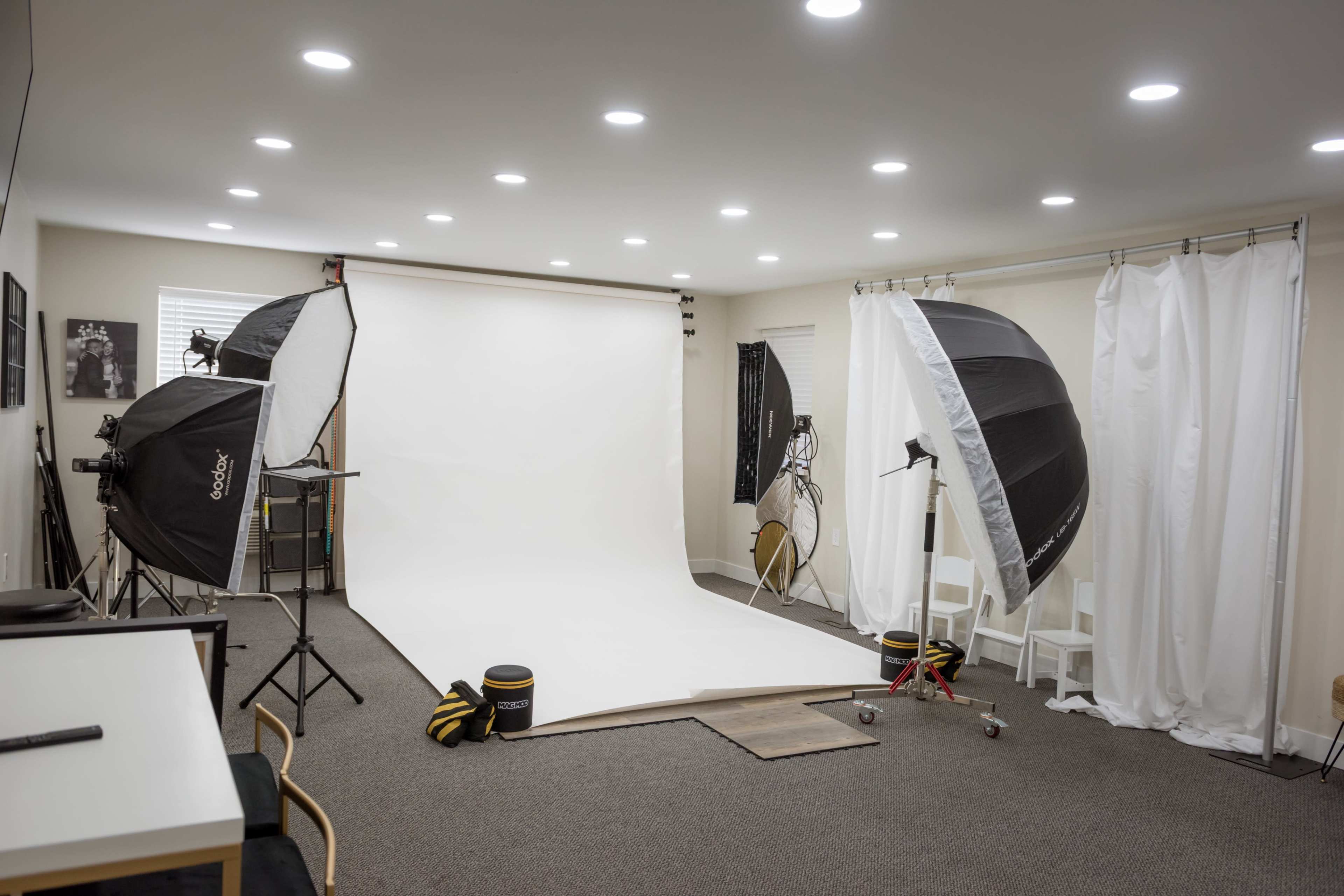A photography studio is equipped with a seamless white backdrop, two large light umbrellas, and various lighting equipment.