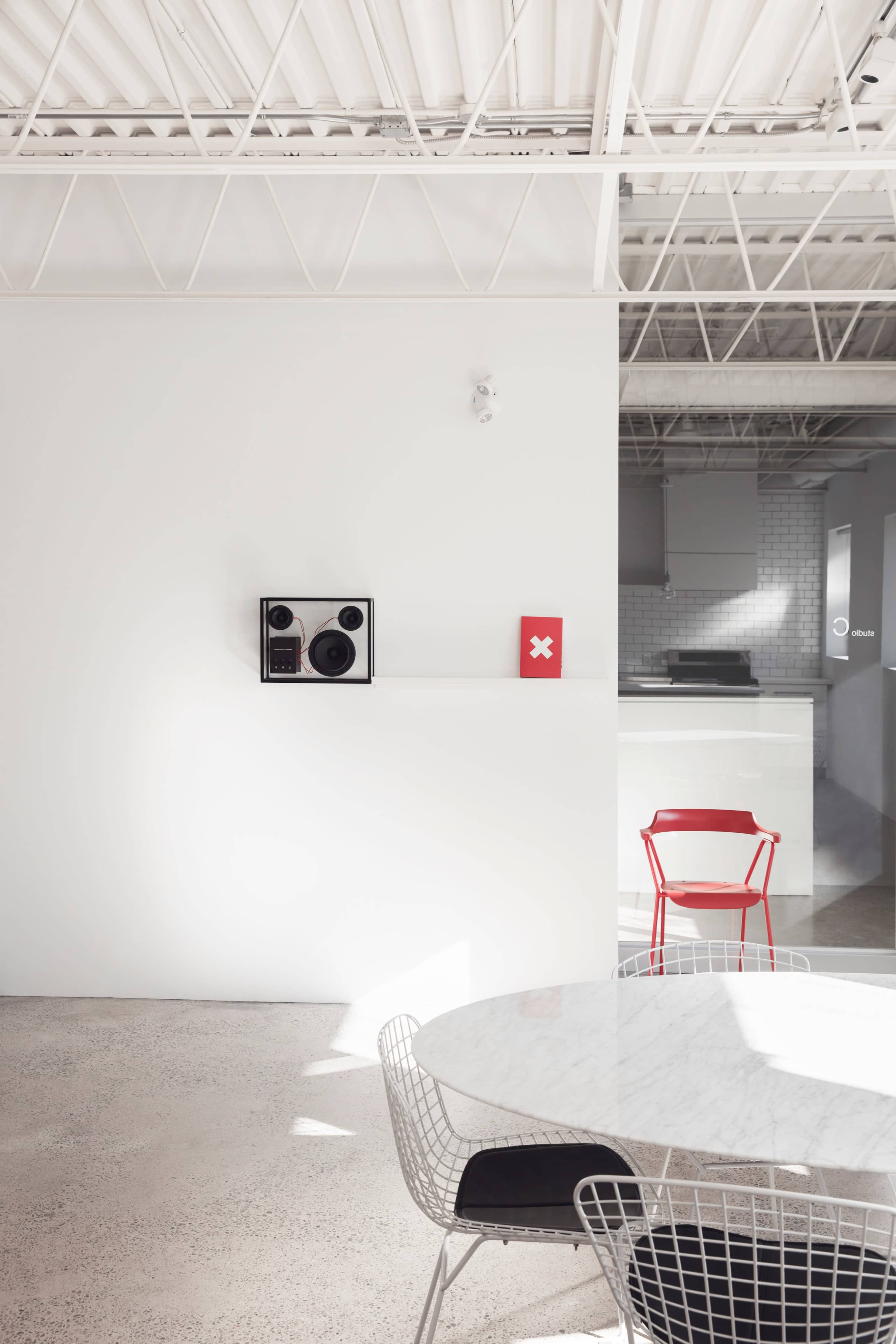 A modern interior features a white wall with a vintage speaker system and a red square decoration, alongside a marble dining table and a red chair in the foreground.