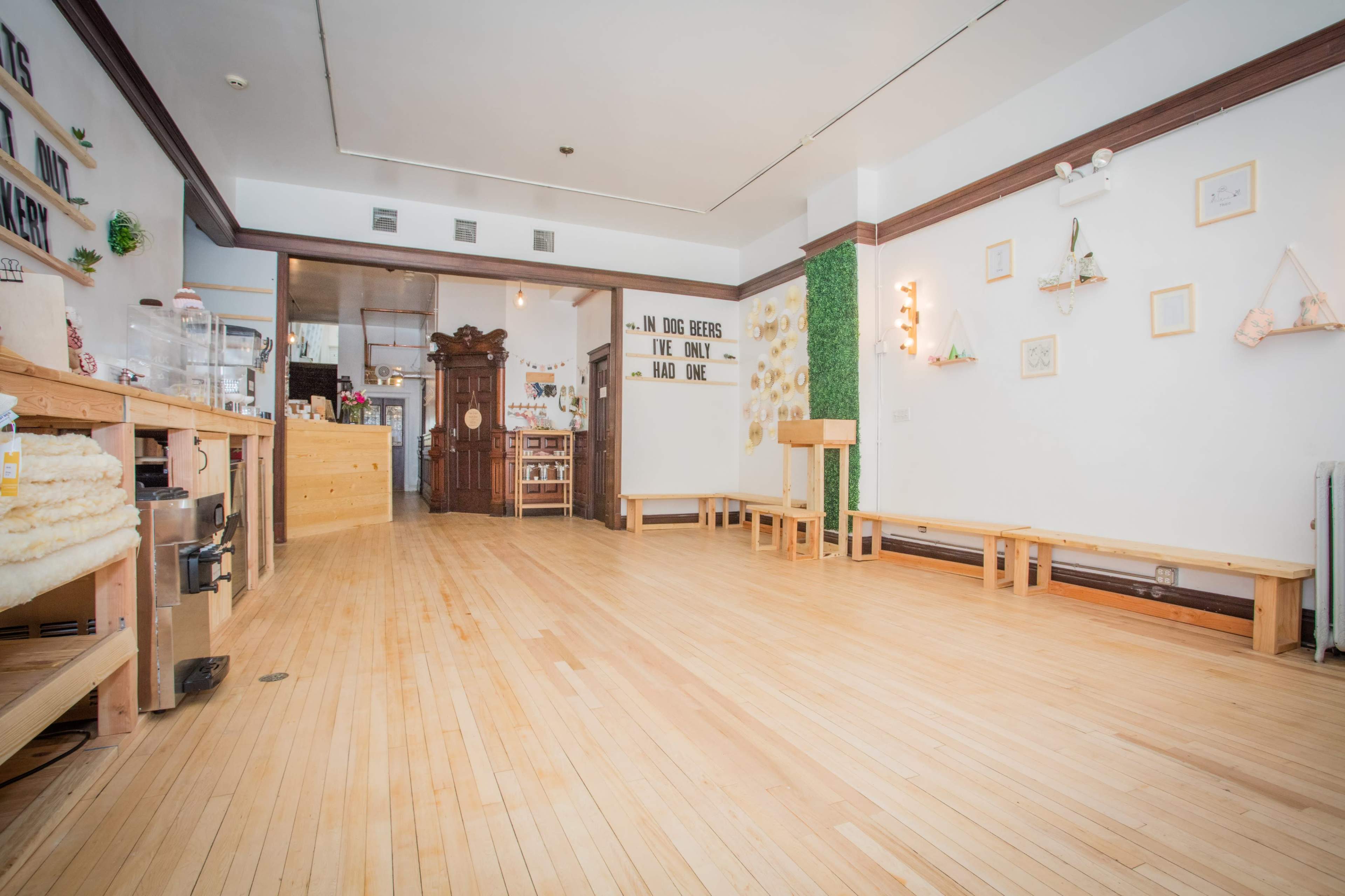 A spacious interior of a cafe with wooden flooring, empty benches, and decorative wall installations.