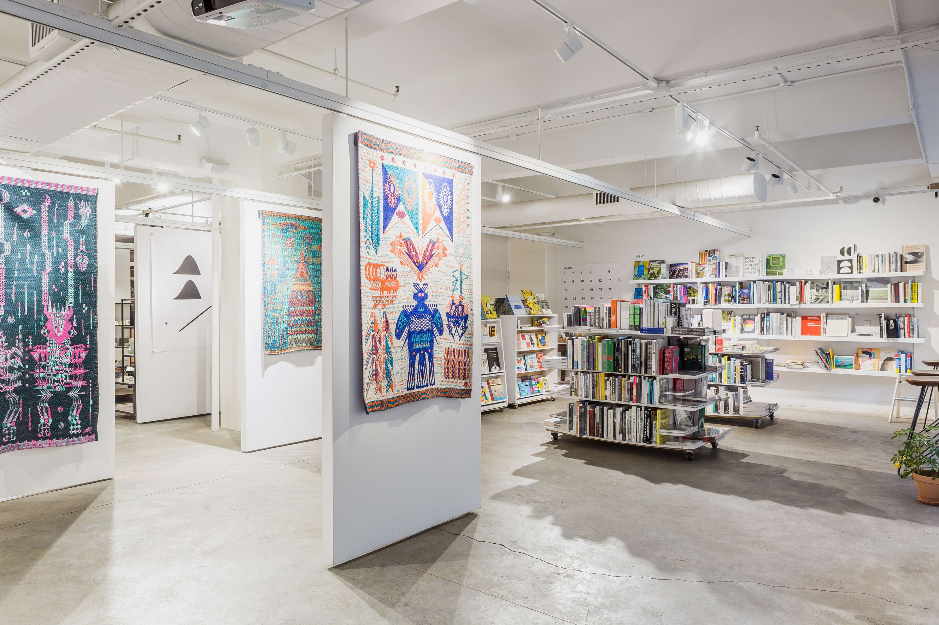 A modern bookstore with shelves of books, colorful wall hangings, and a spacious layout illuminated by overhead lighting.