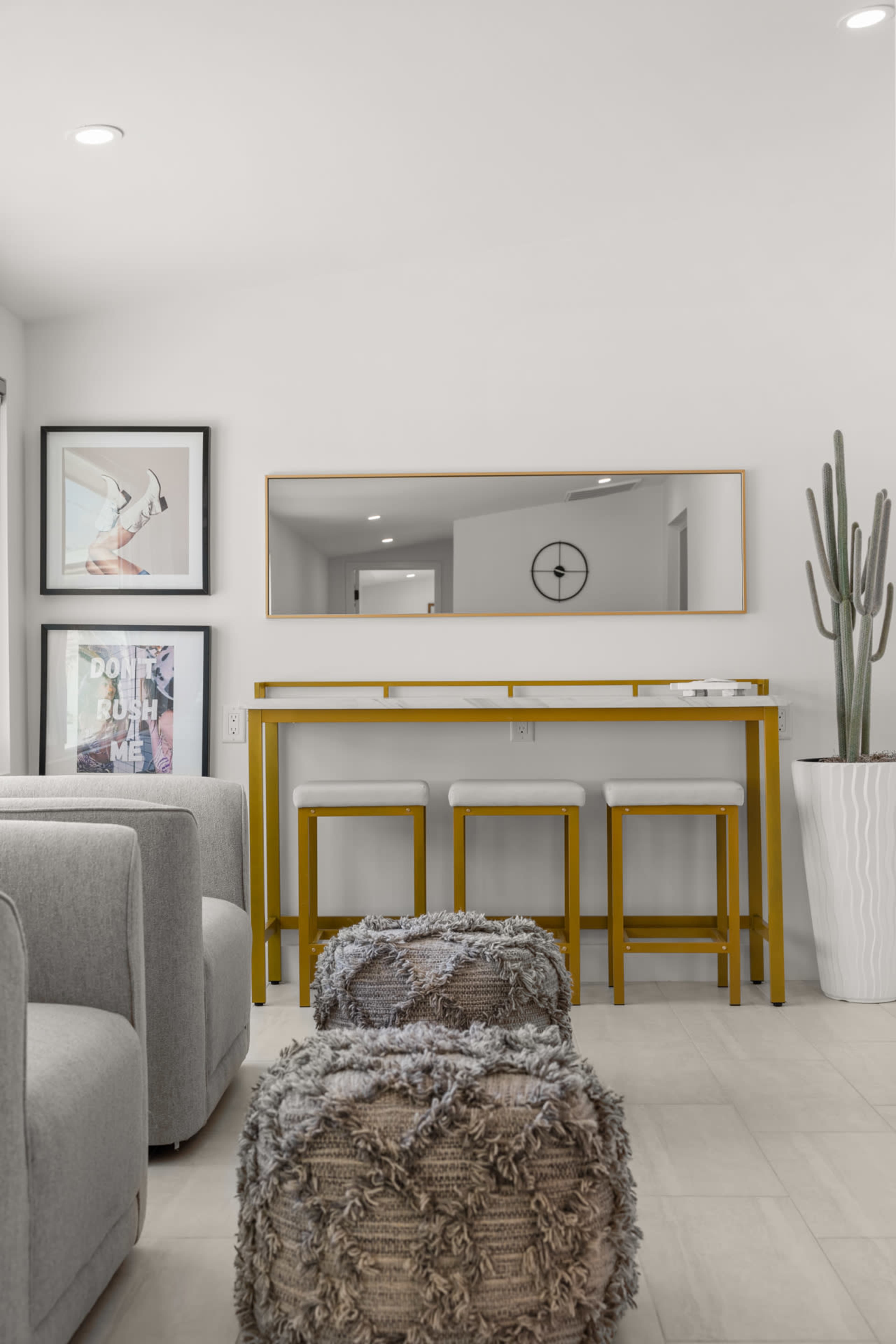 A minimalist interior featuring a yellow bar table with three stools, a large mirror, and a decorative cactus in a modern planter.