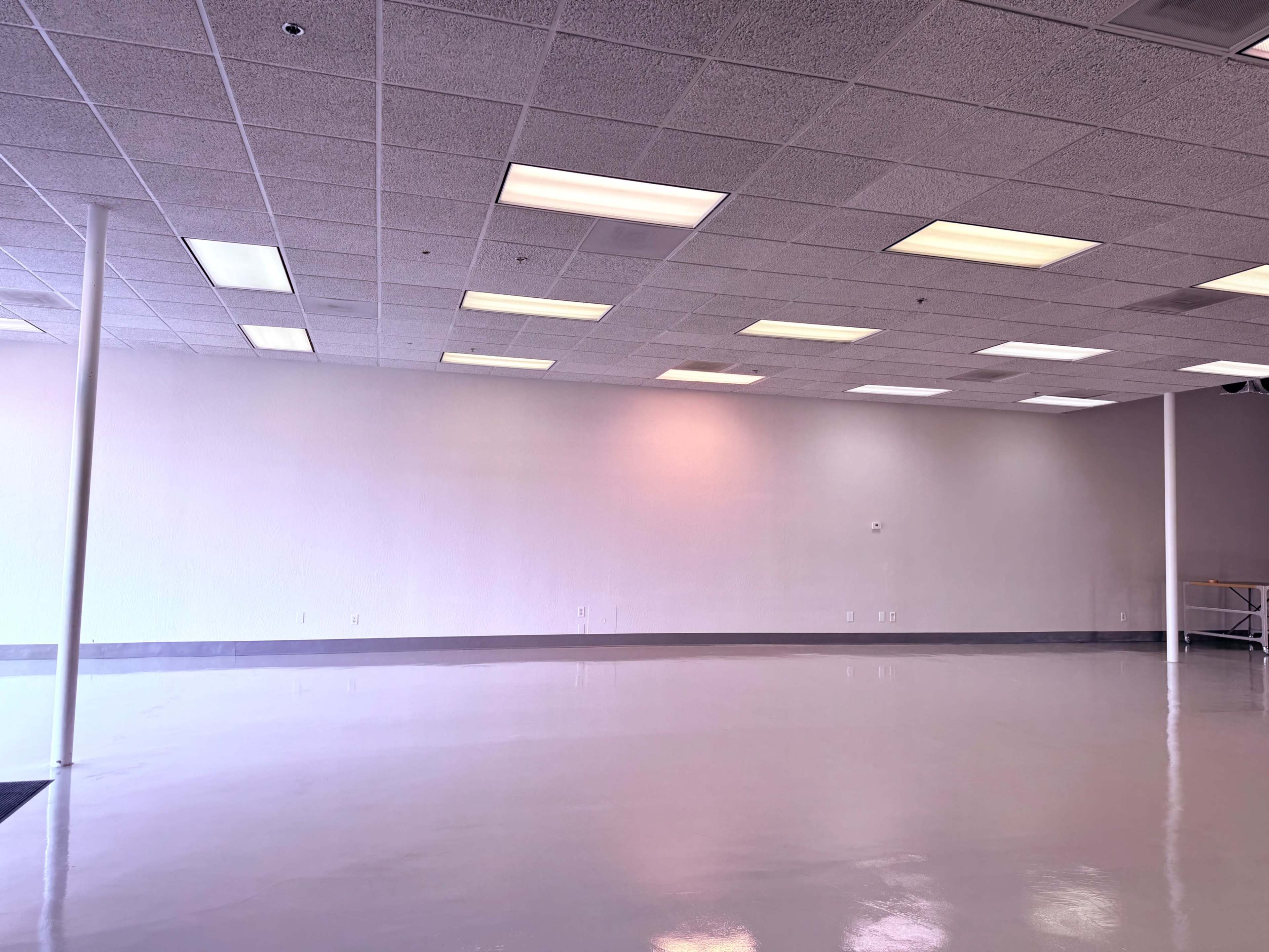 The image shows an empty room with a smooth, shiny floor and fluorescent ceiling lights, featuring plain white walls and minimal furnishings.