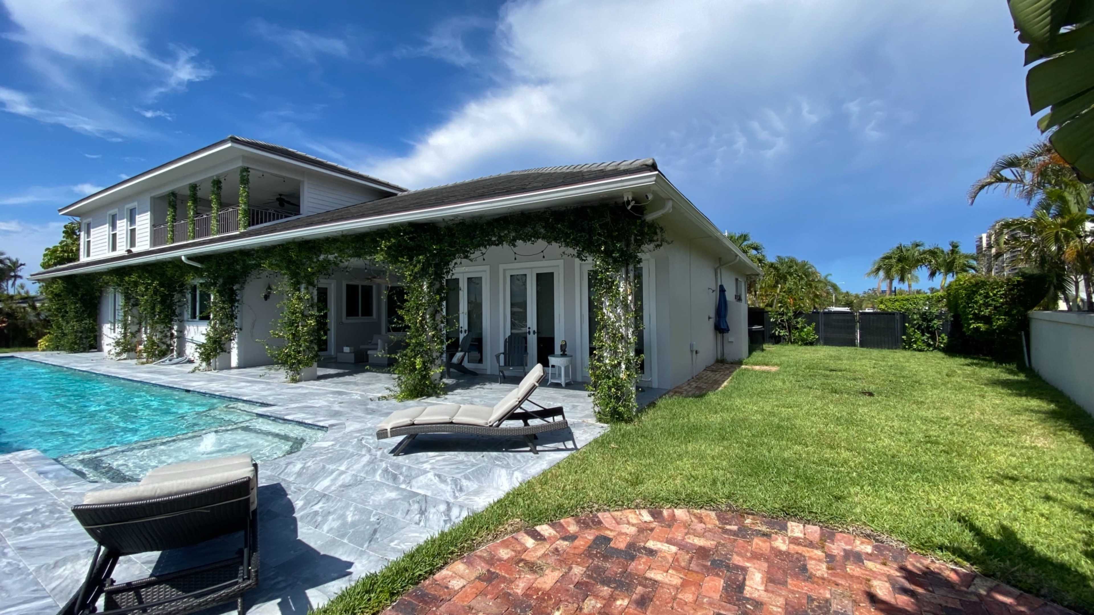 A modern two-story house with a swimming pool and lounge chairs is surrounded by greenery and a well-maintained lawn.
