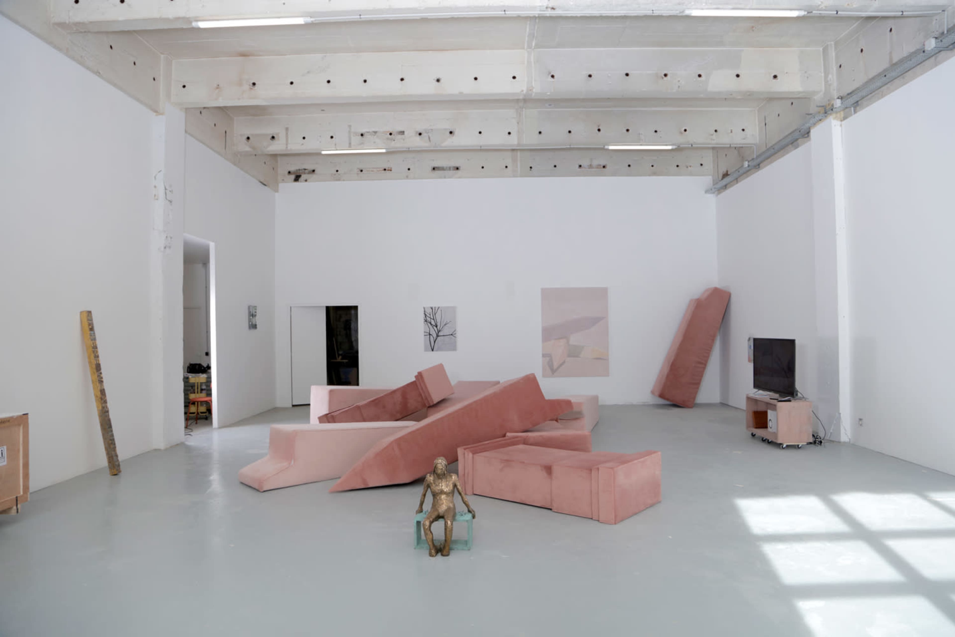 A spacious, minimalistic room with pink furniture arranged in an unconventional manner and a small sculpture positioned in front.