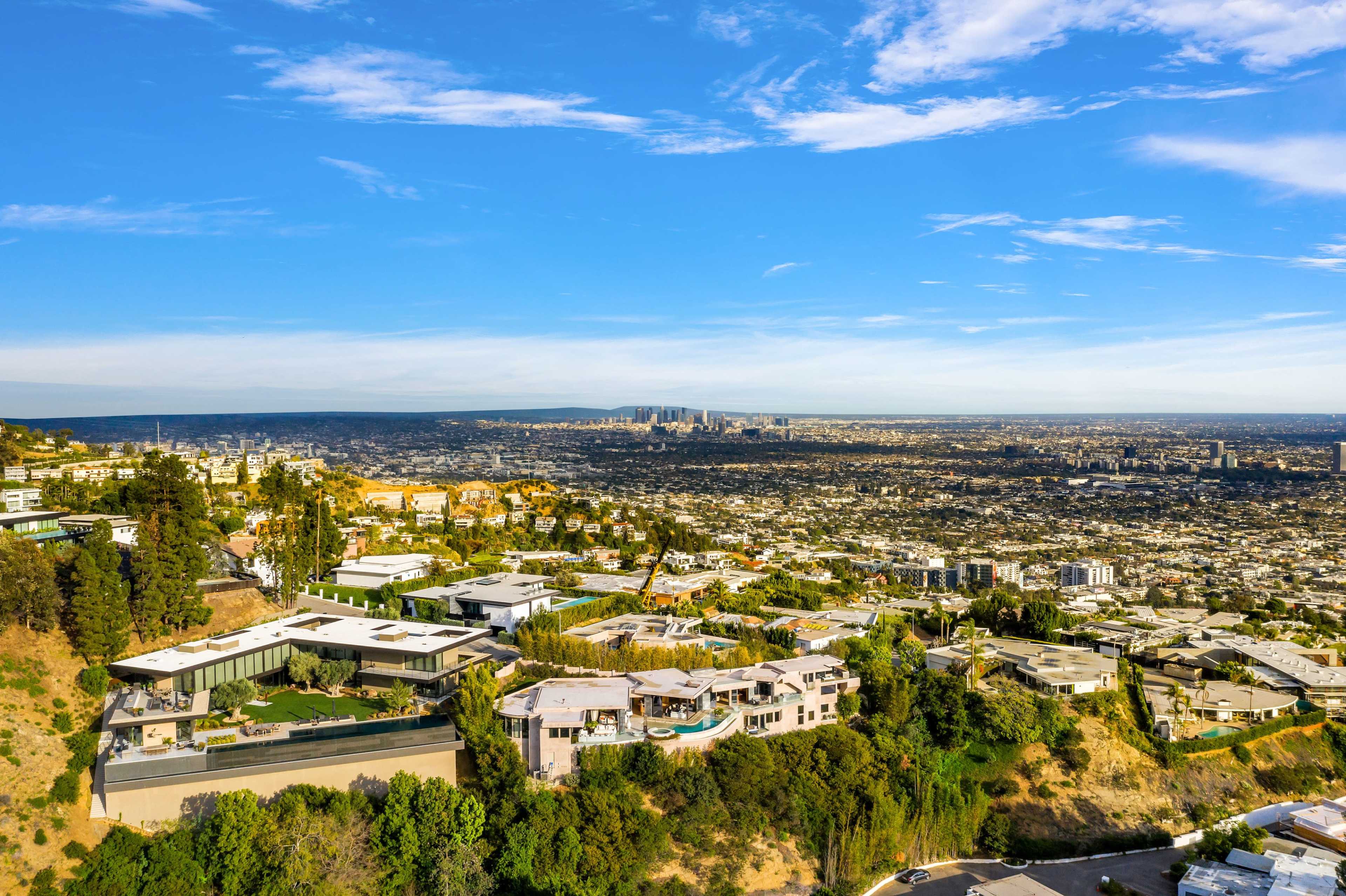 A sprawling hillside residential area with modern homes overlooking a cityscape under a clear blue sky.