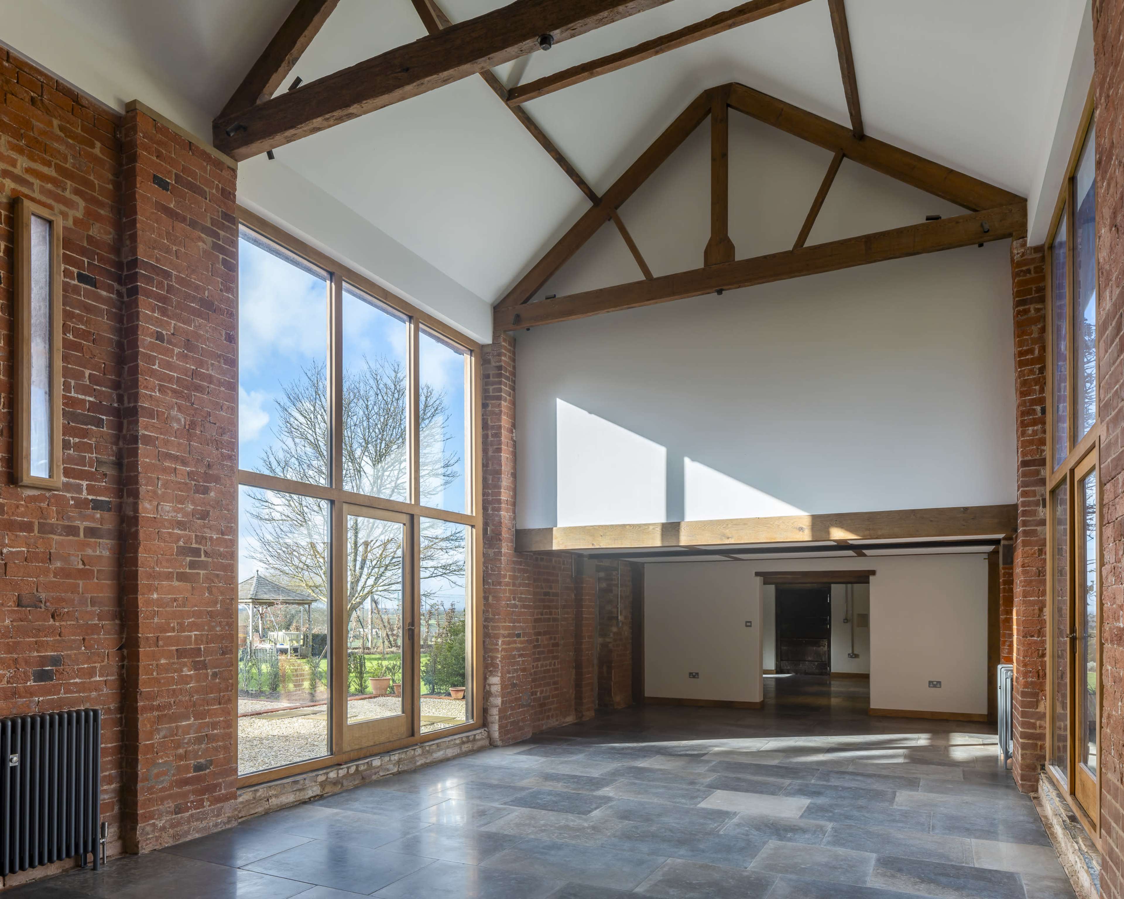 The image shows a spacious interior of a building with exposed brick walls, large windows, and a high vaulted ceiling supported by wooden beams.