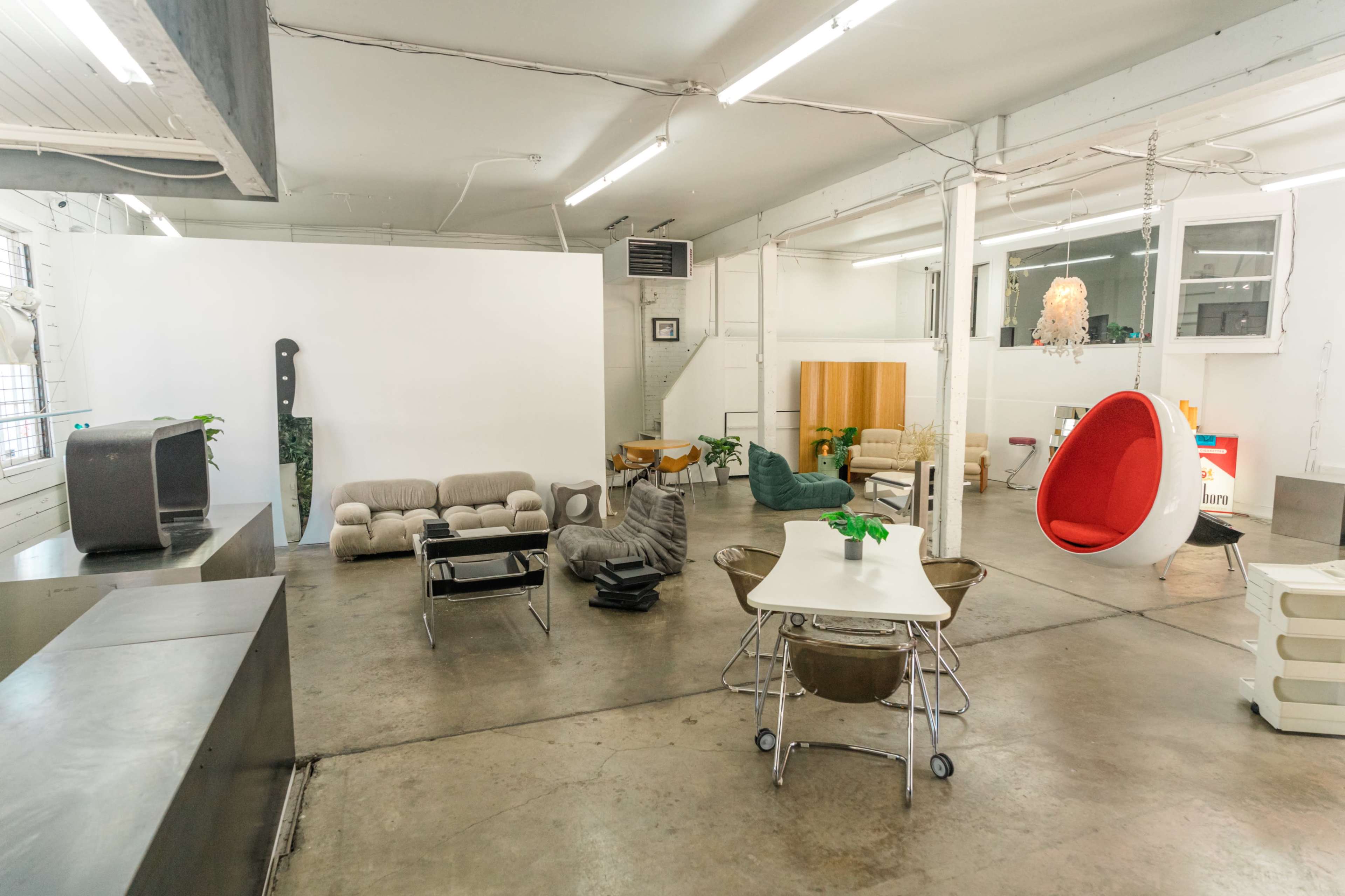 A spacious, minimalist interior filled with various modern furniture pieces, including couches, a hanging chair, and a dining table.
