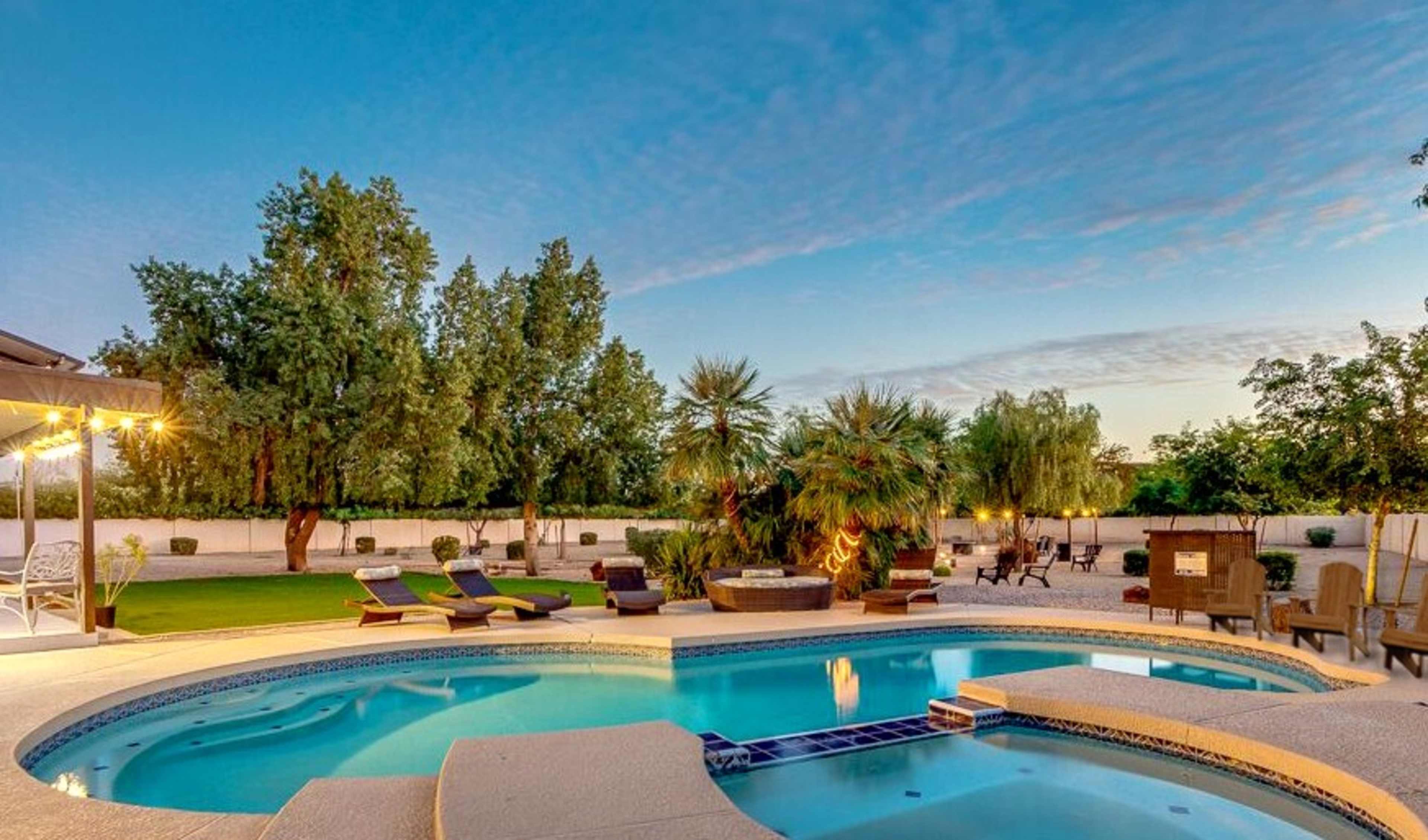 A swimming pool surrounded by lounge chairs and palm trees in a spacious backyard.