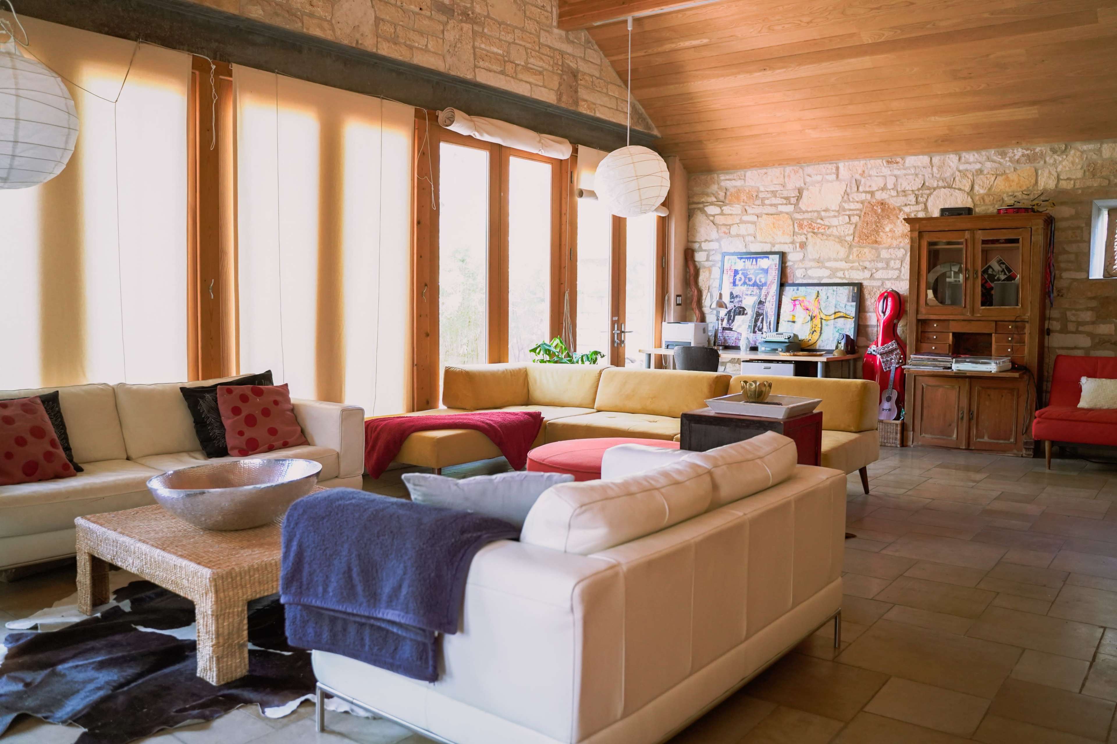 A spacious living room features colorful sofas, large windows, and a mix of natural stone and wooden elements.