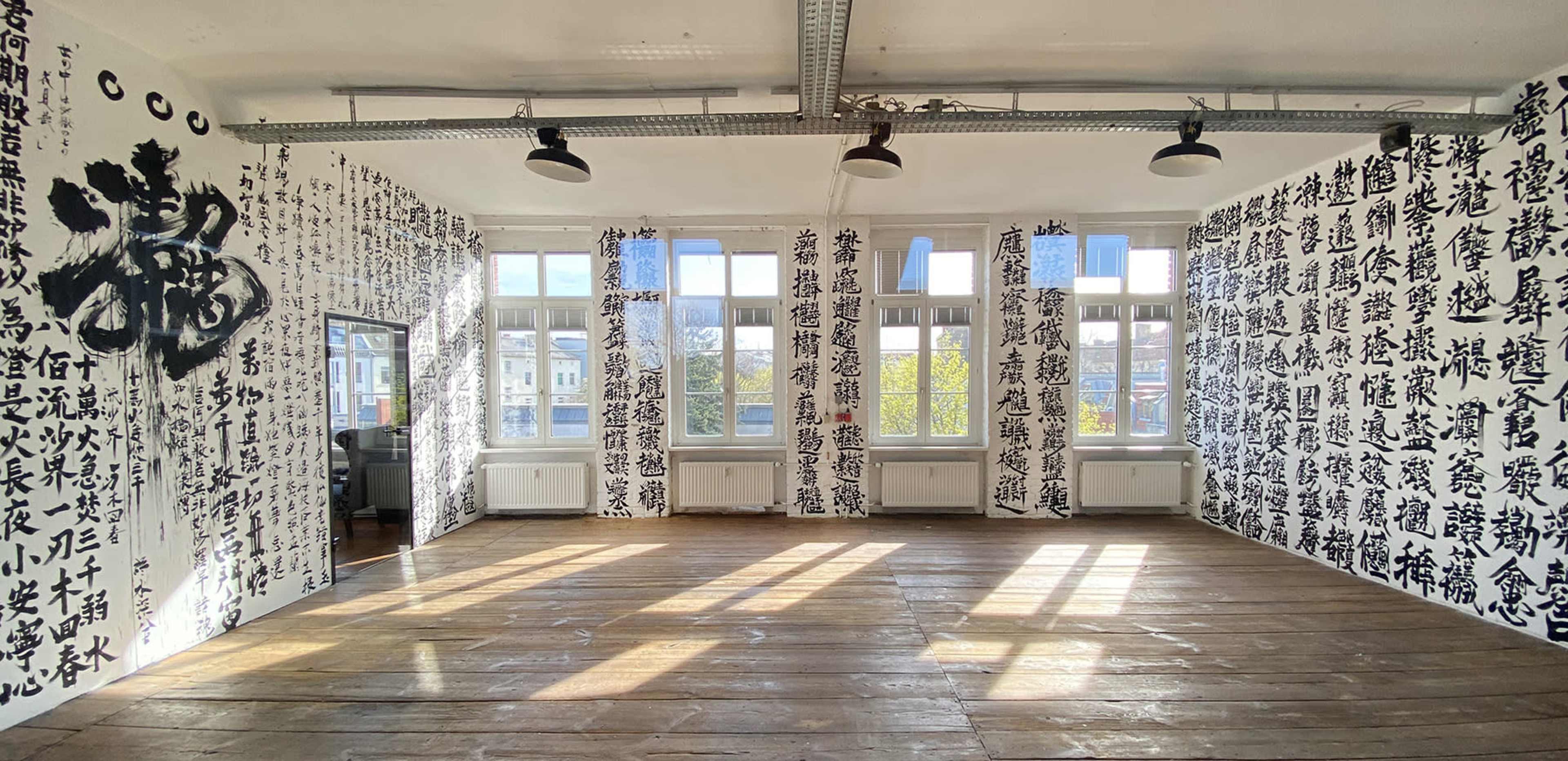 An empty room with large windows and walls covered in black calligraphy against a white background.