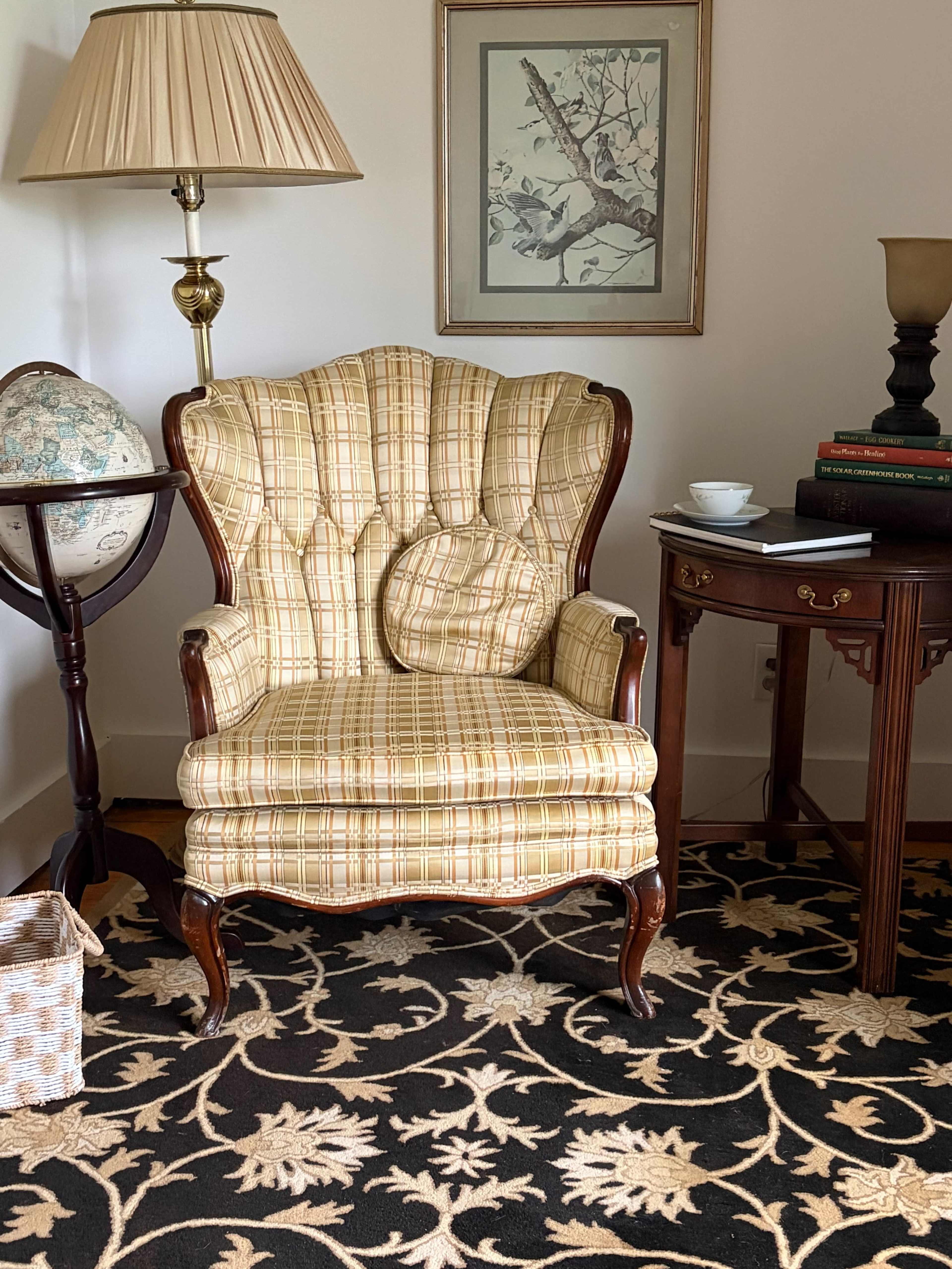 The image shows a patterned armchair with a matching pillow, positioned near a lamp and a small side table in a room with a globe and artwork on the wall.