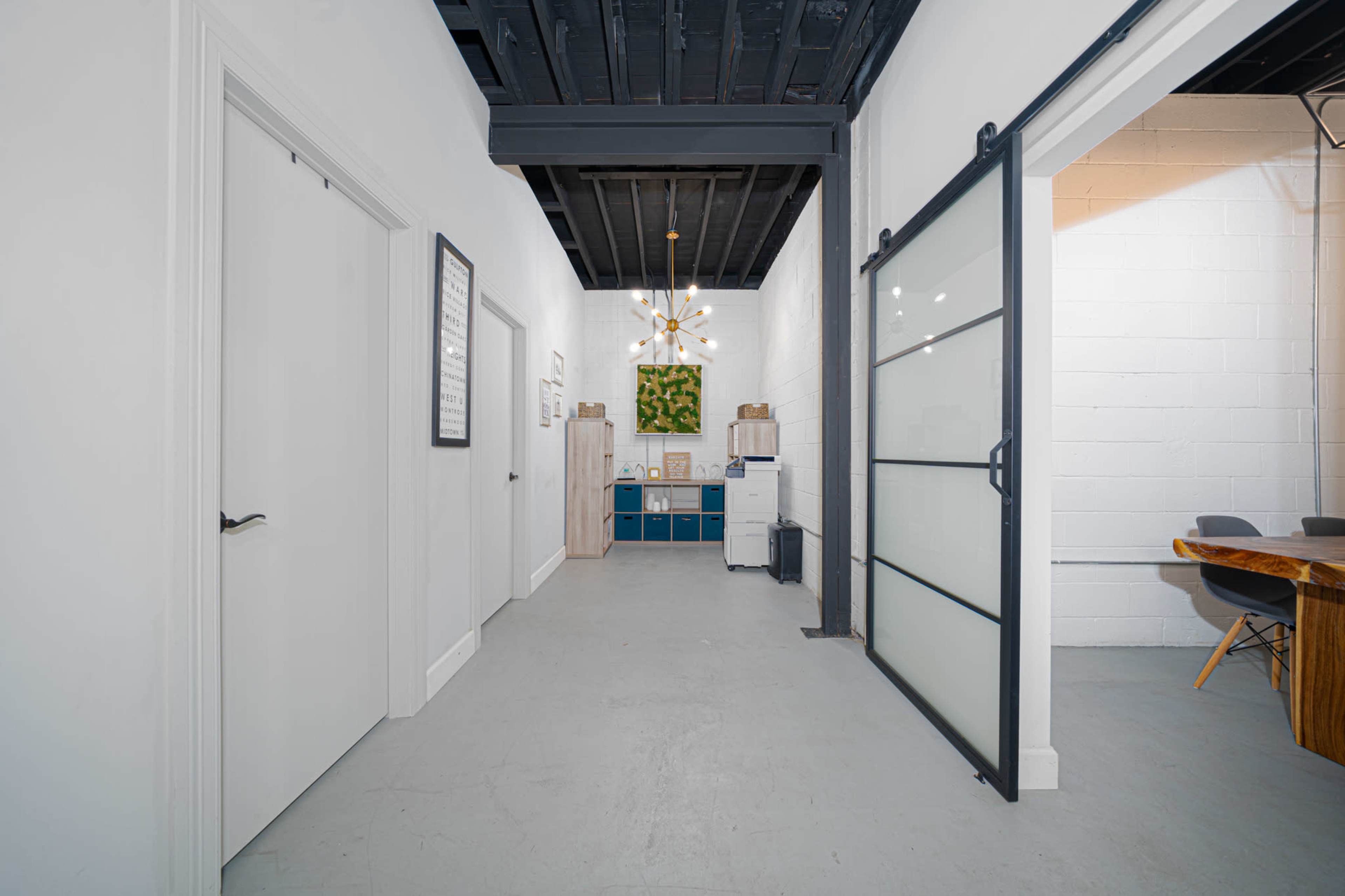 A long corridor features a sliding glass door on one side, with a kitchenette and seating area visible at the end.