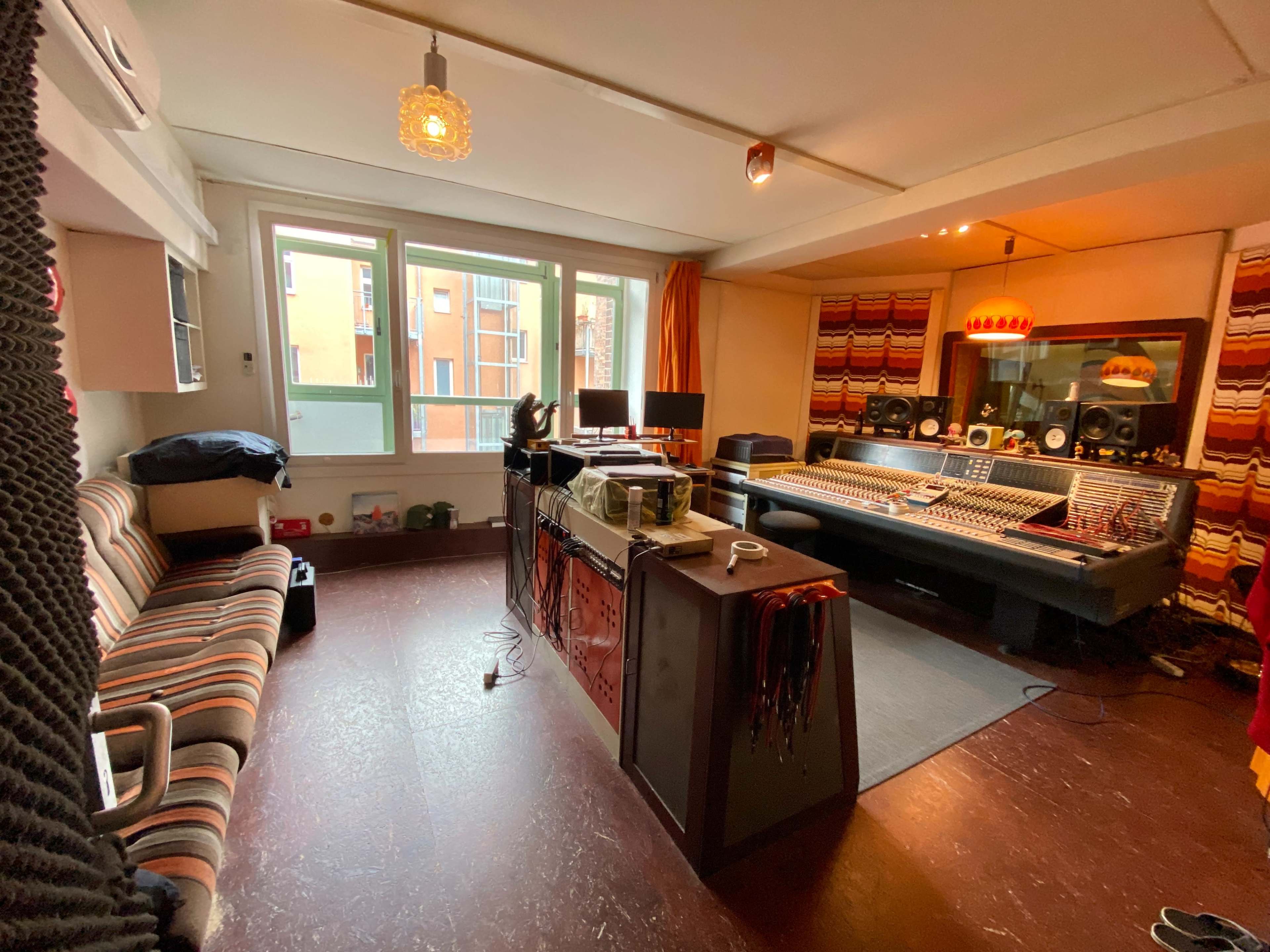 A recording studio featuring a large mixing console, computer monitors, and seating arranged in a corner with patterned upholstery.