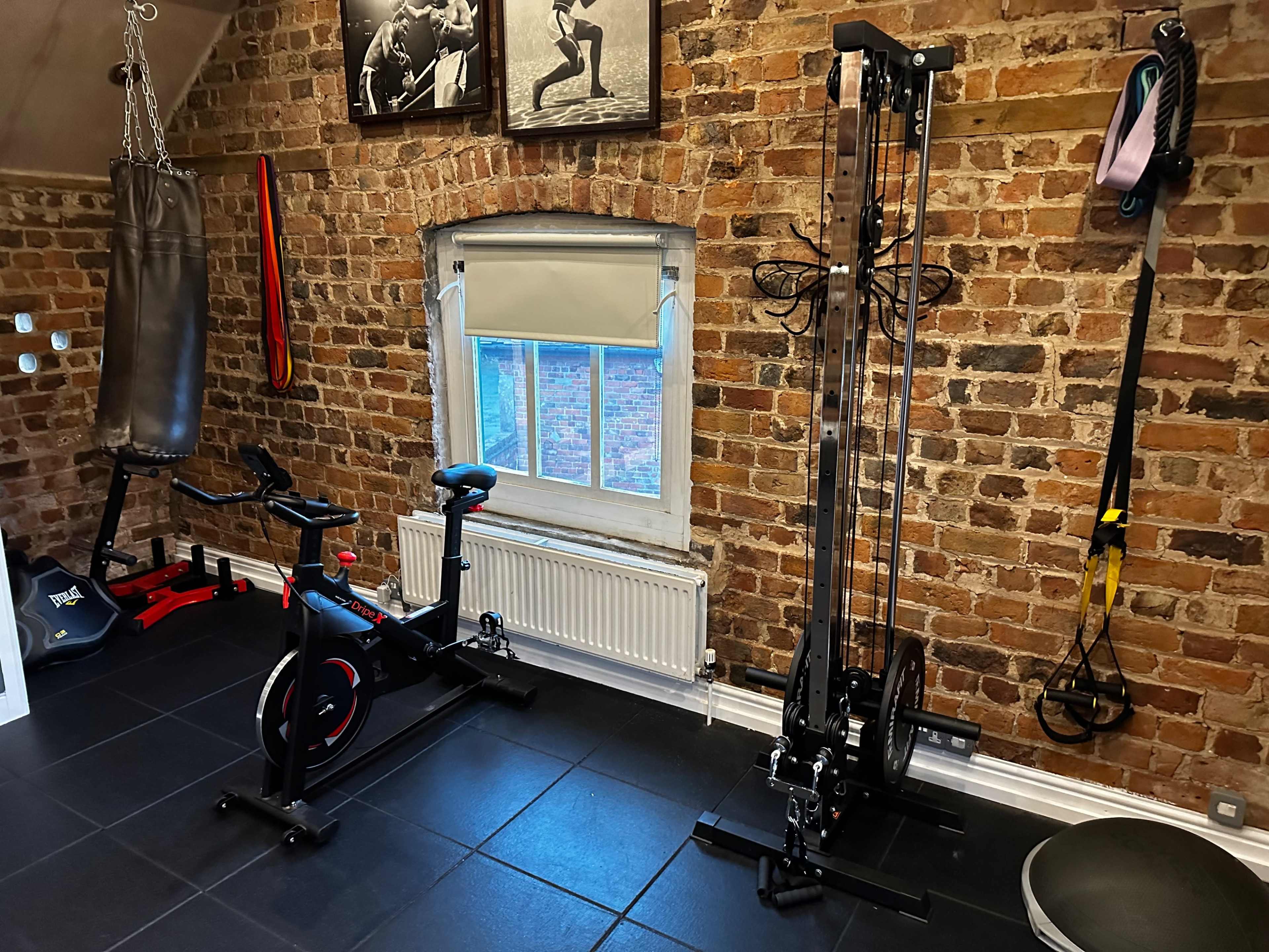A home gym with a stationary bike, a cable machine, a punching bag, and a window on a brick wall.