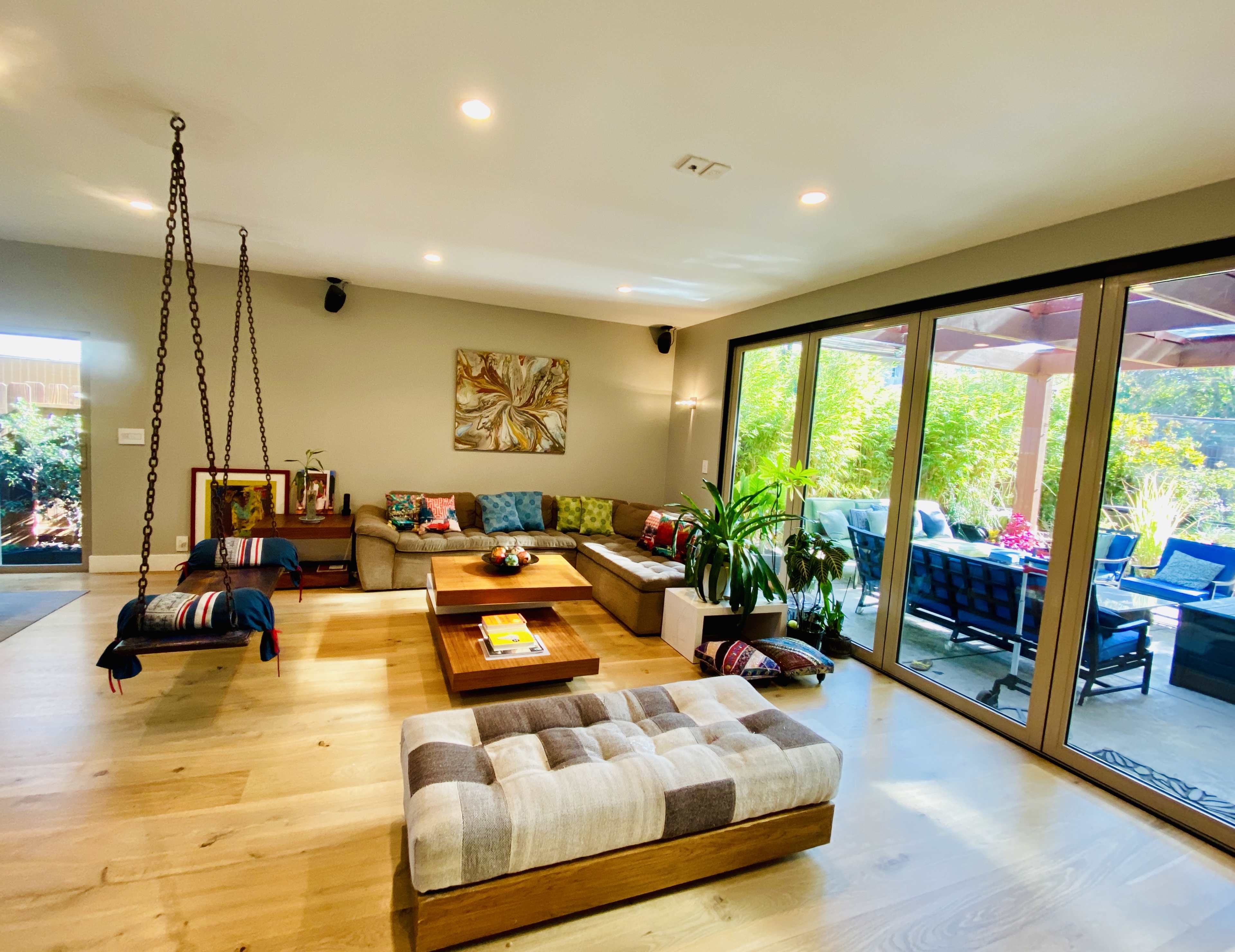 The room features a spacious living area with a swing seat, a coffee table, and large windows overlooking a patio garden.