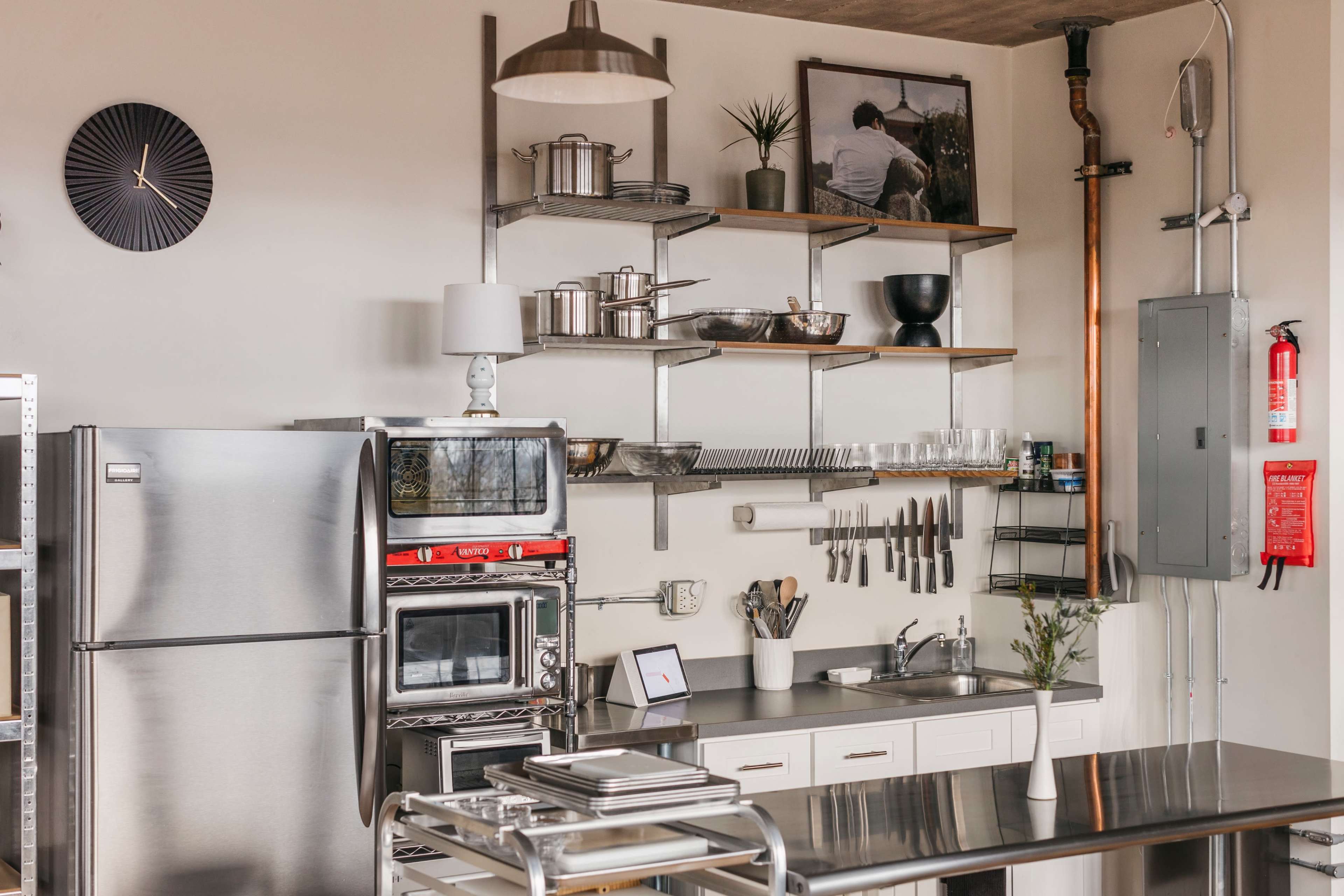 A modern kitchen features stainless steel appliances, open shelving with cookware, and a clean countertop setup.
