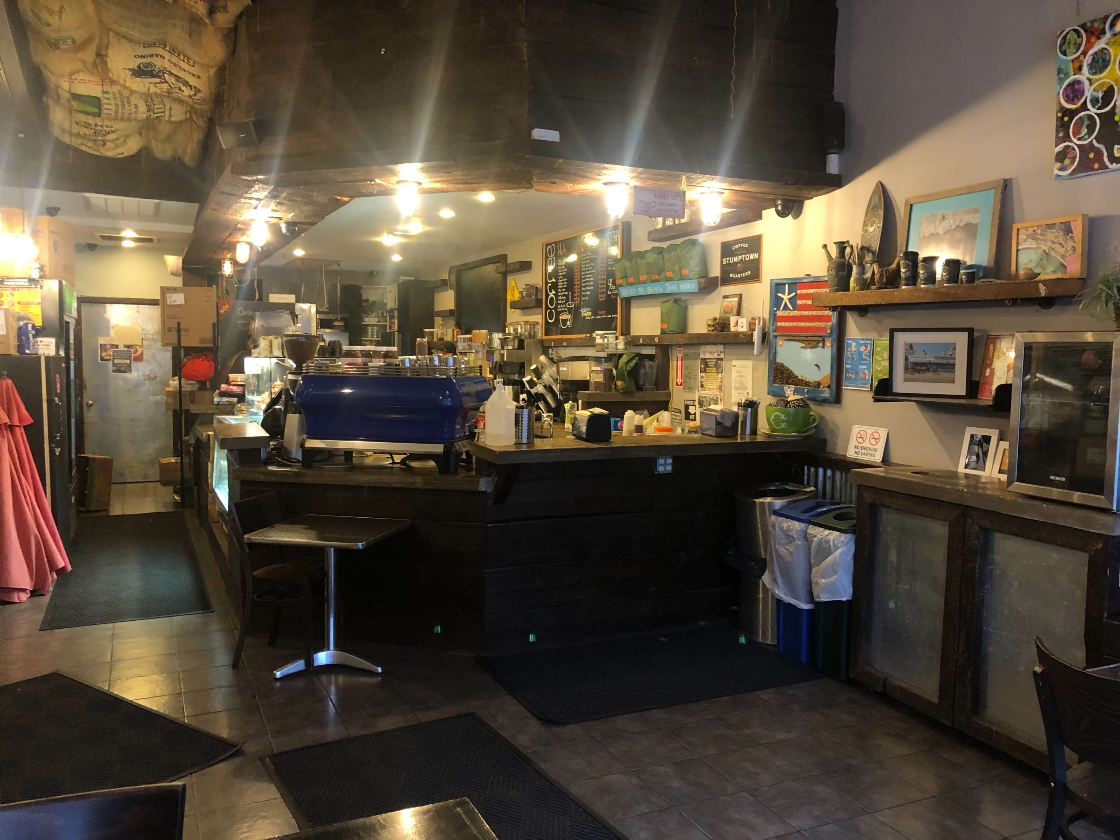 A cozy café interior with a wooden counter, a blue espresso machine, and seating areas.