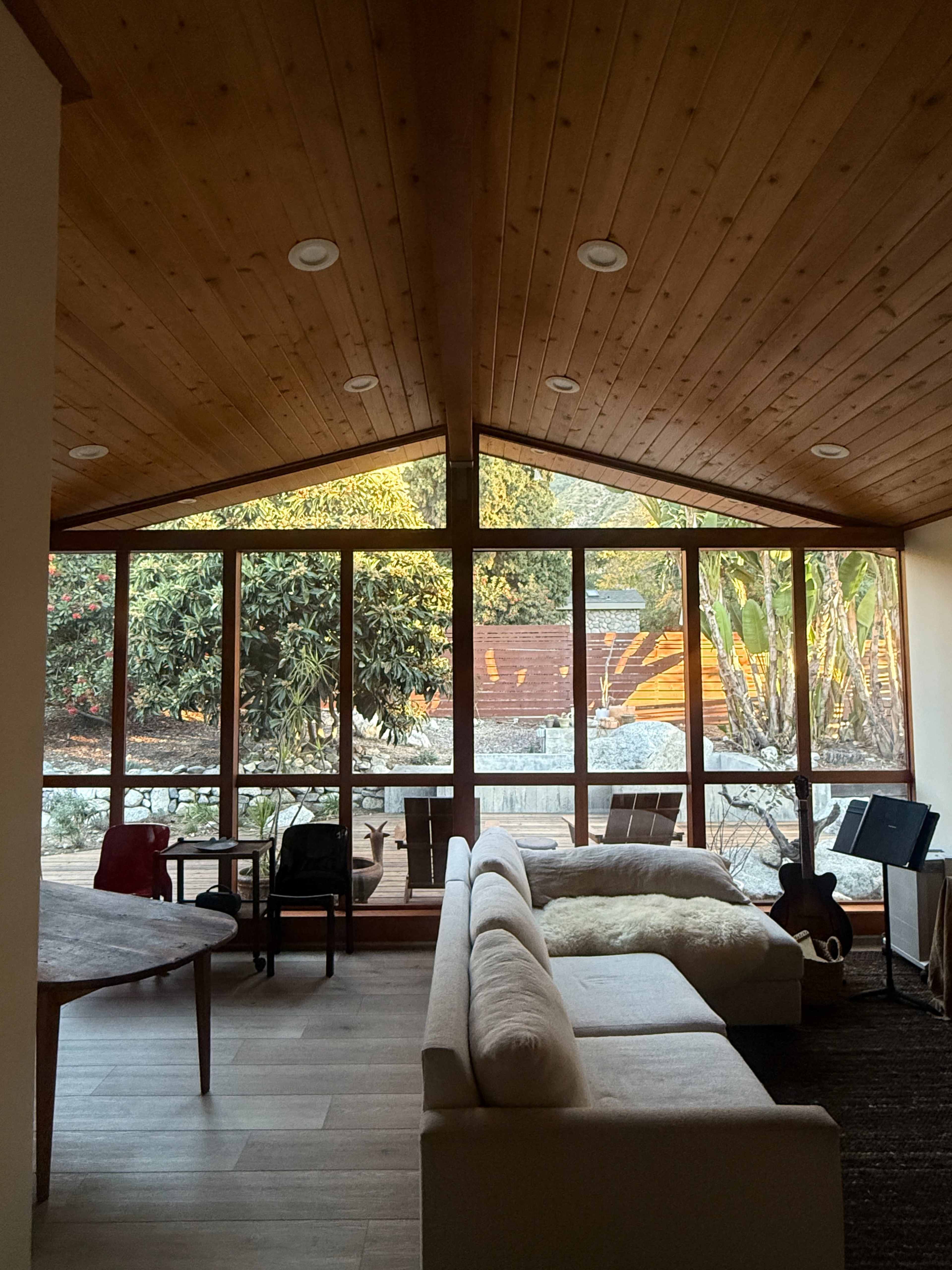 A spacious living room features a wooden ceiling and large windows looking out onto a garden.