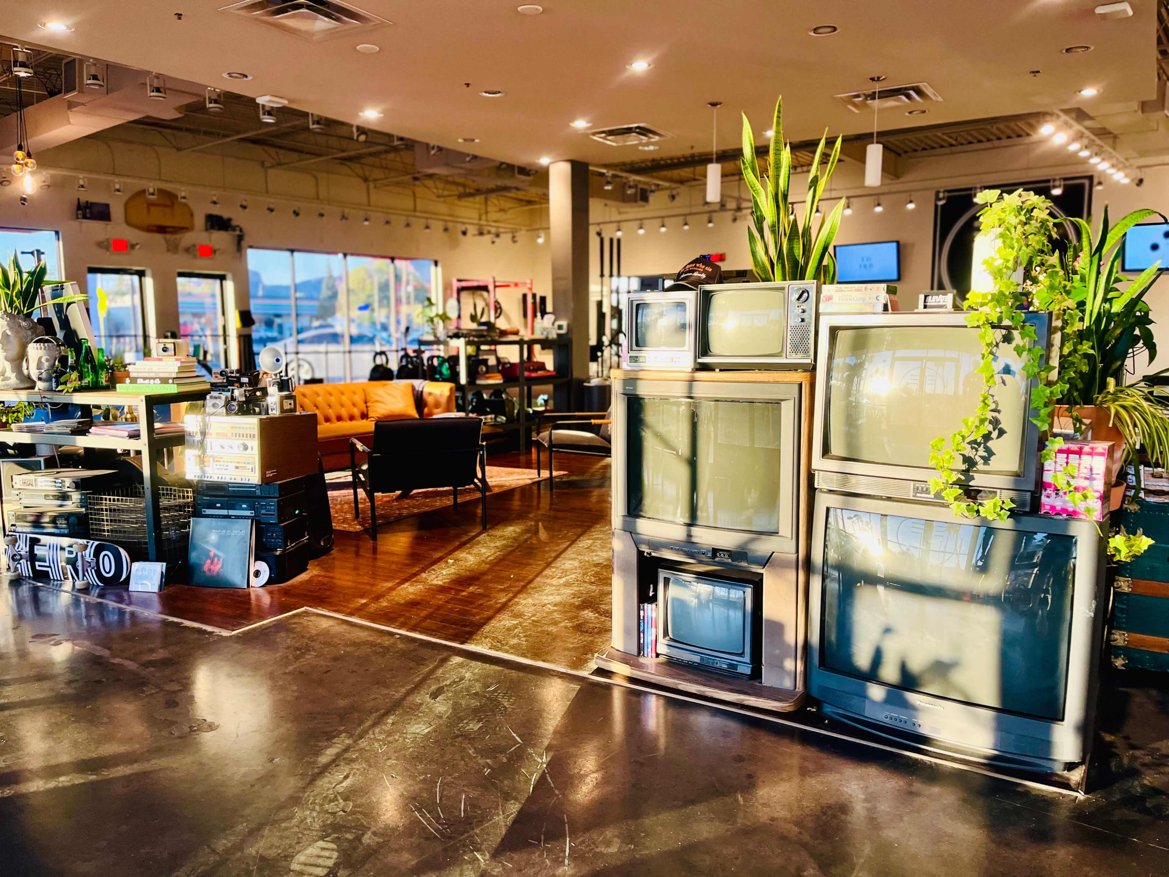 The interior of a vintage store features several retro televisions displayed alongside modern furniture and potted plants.