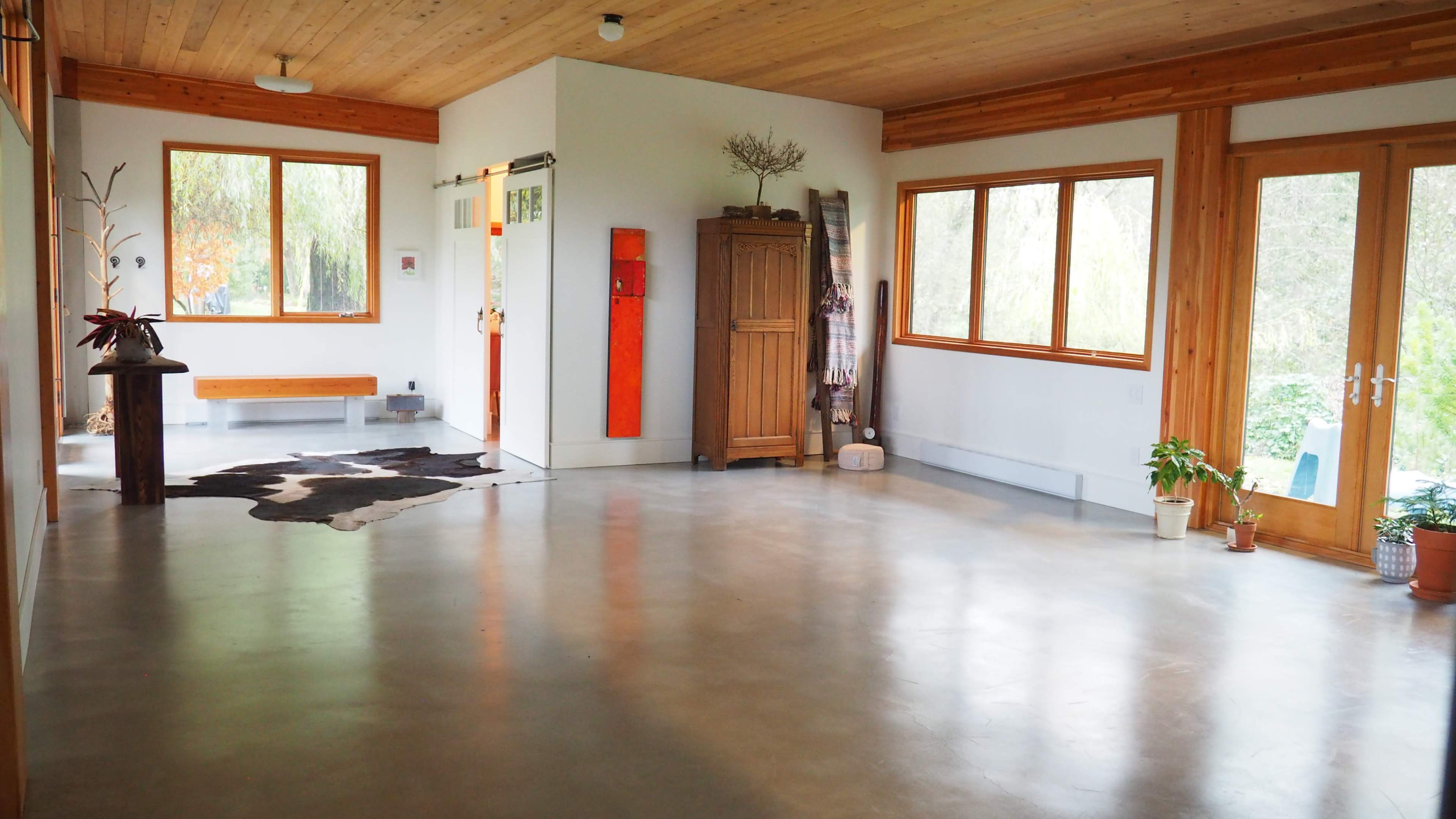 A spacious, modern interior with a polished concrete floor, wooden ceilings, large windows, and minimalistic furniture.