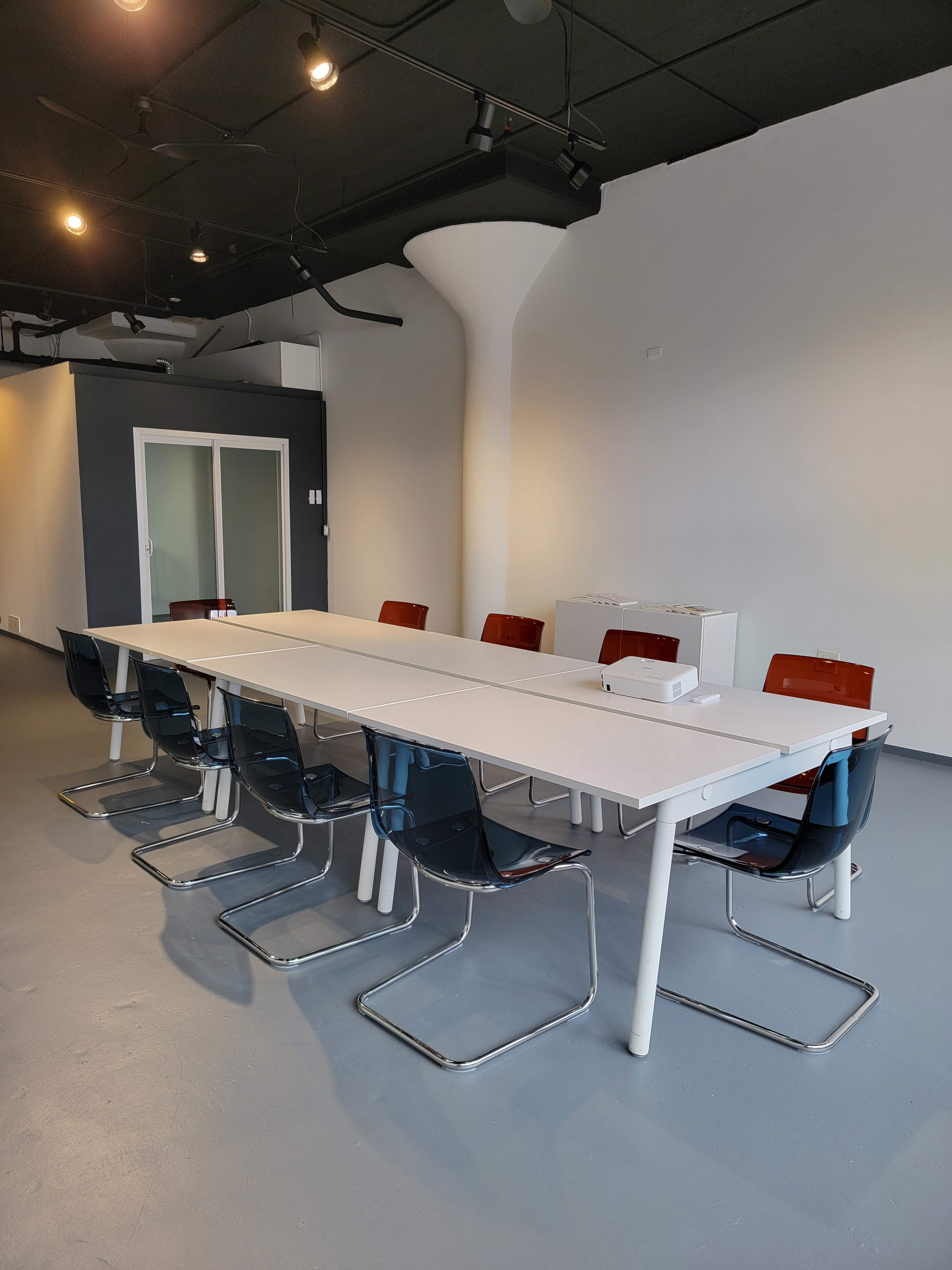 A large, modern conference table is surrounded by transparent chairs in a minimalistic room with a gray floor and white walls.
