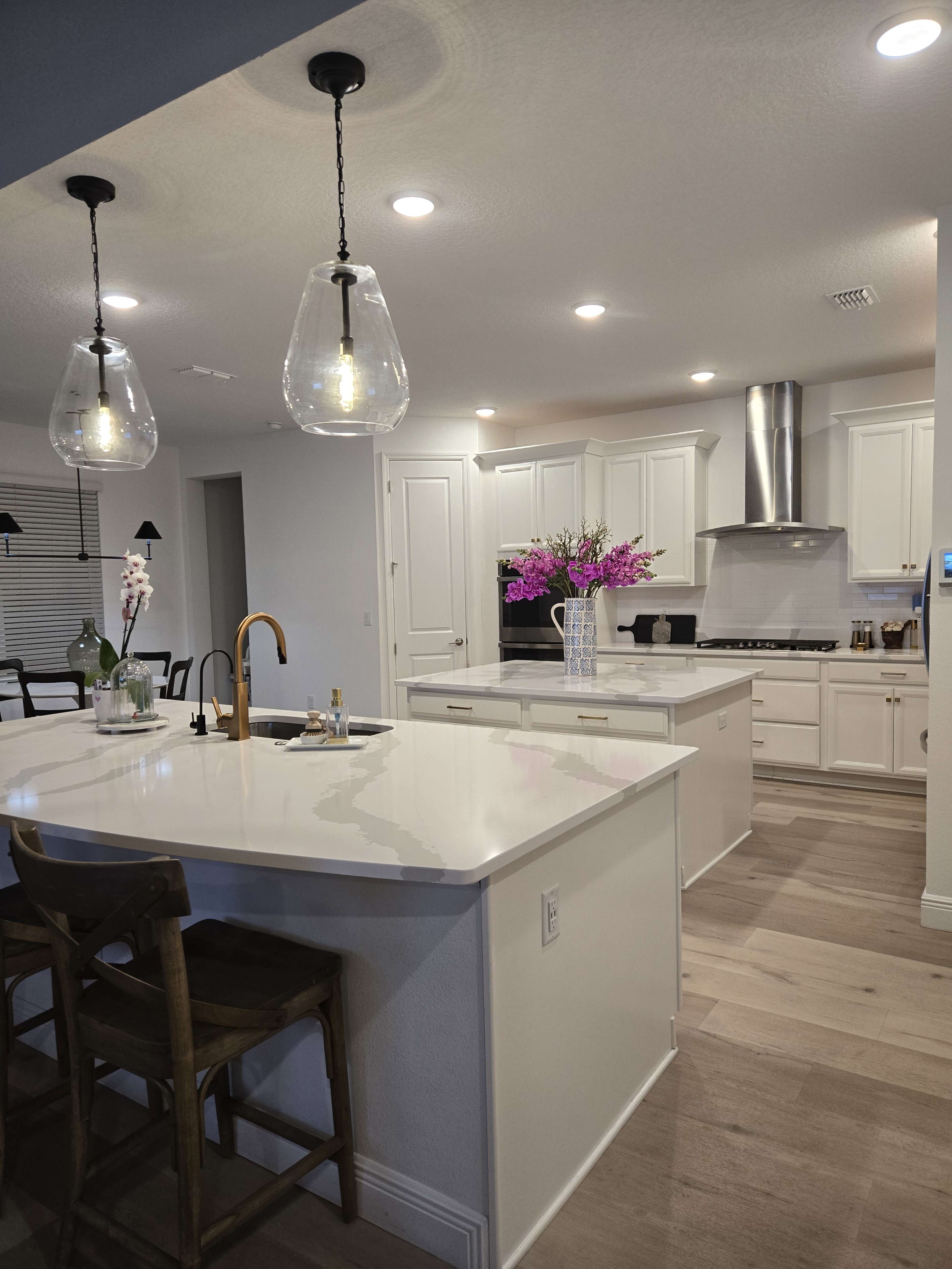The image shows a modern kitchen with white cabinetry, a large island with a sink, and pendant lighting above.