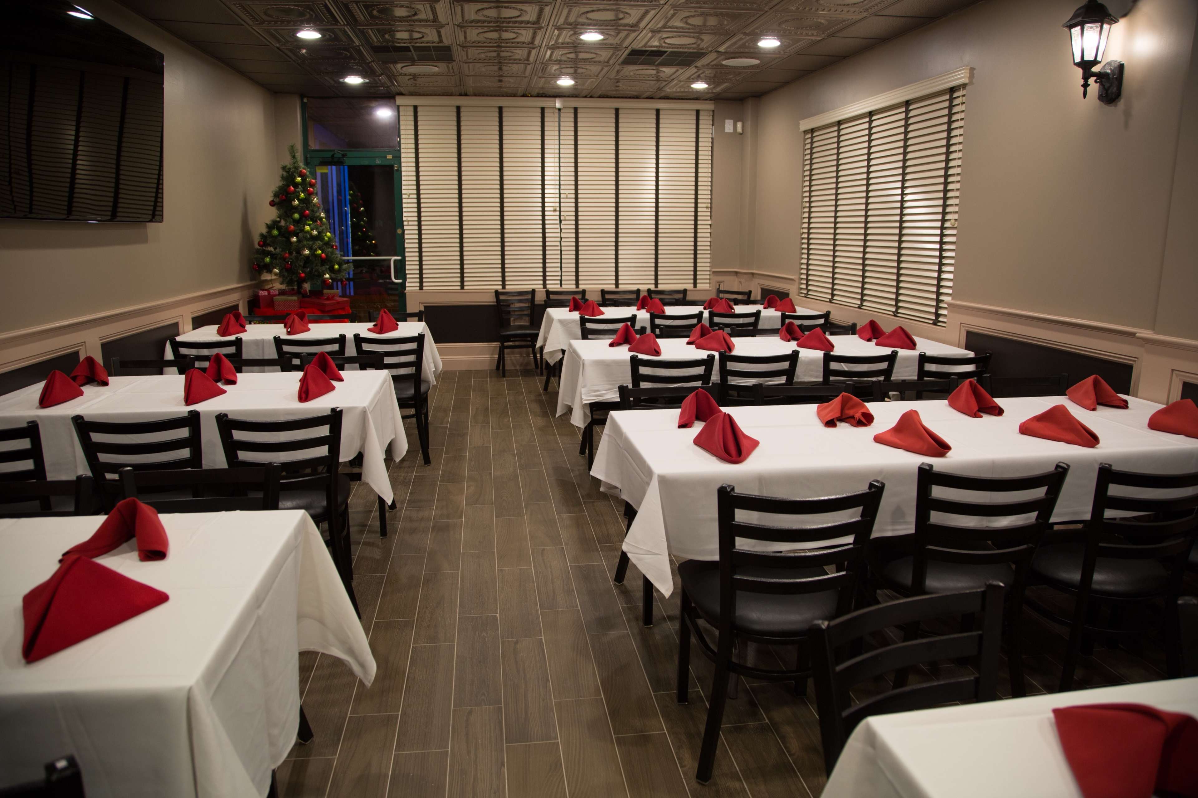 The image shows a restaurant dining area with several tables covered in white tablecloths, each adorned with red napkins, and decorated with a Christmas tree in the corner.