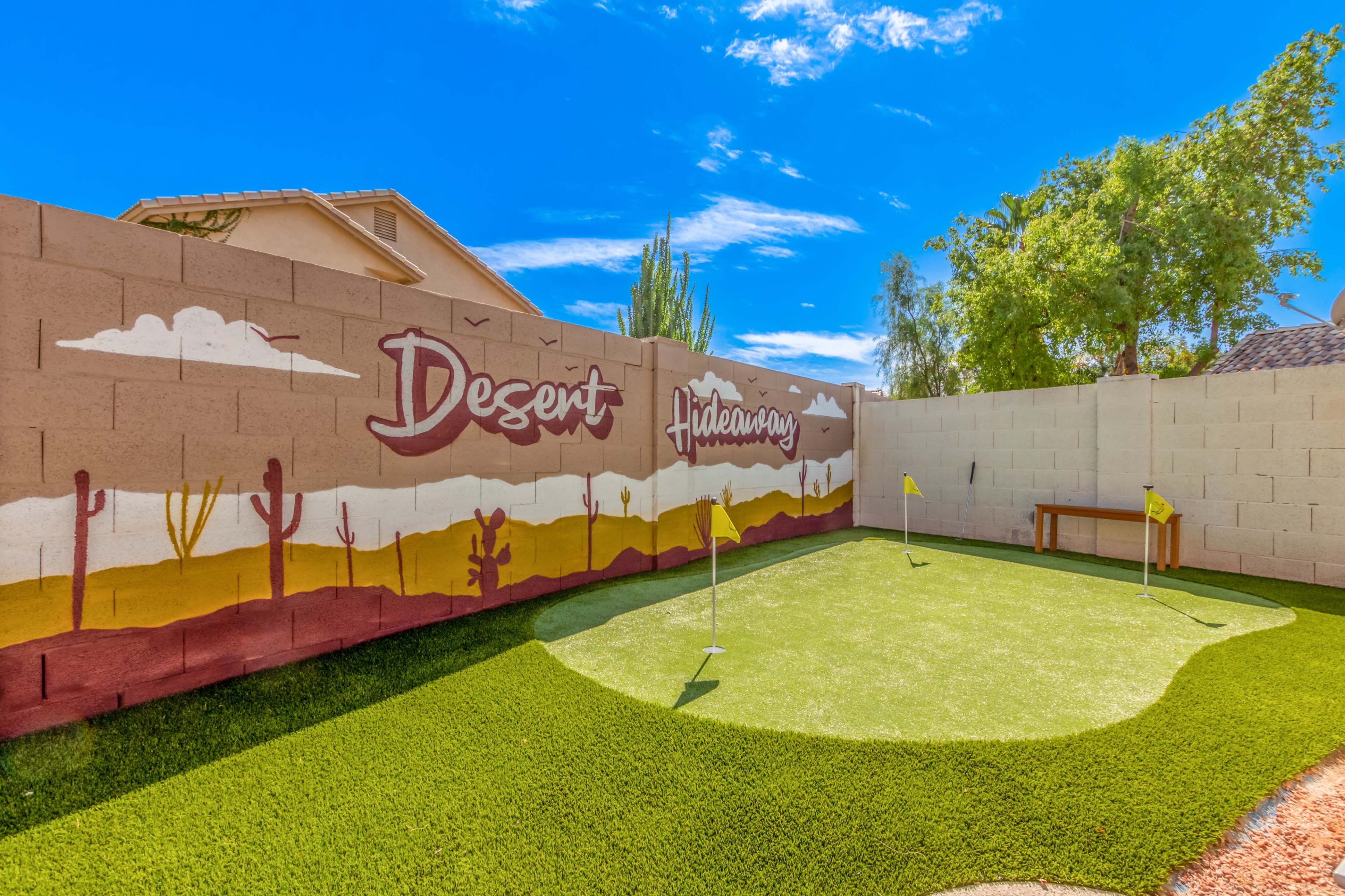 A small putting green surrounded by a painted wall featuring a desert landscape and the words "Desert Hideaway."