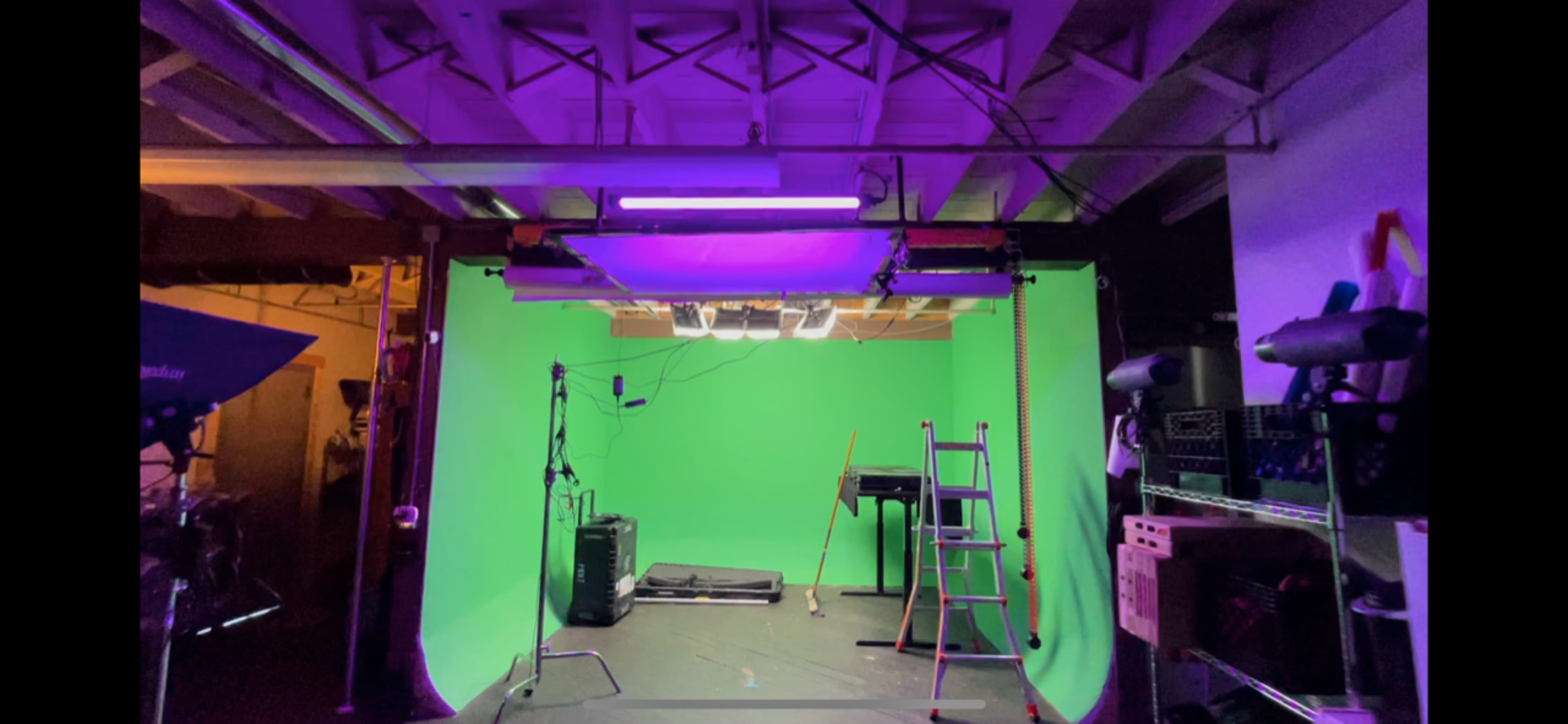 A studio setup with a green screen, lighting equipment, a ladder, and various props arranged in a spacious room.