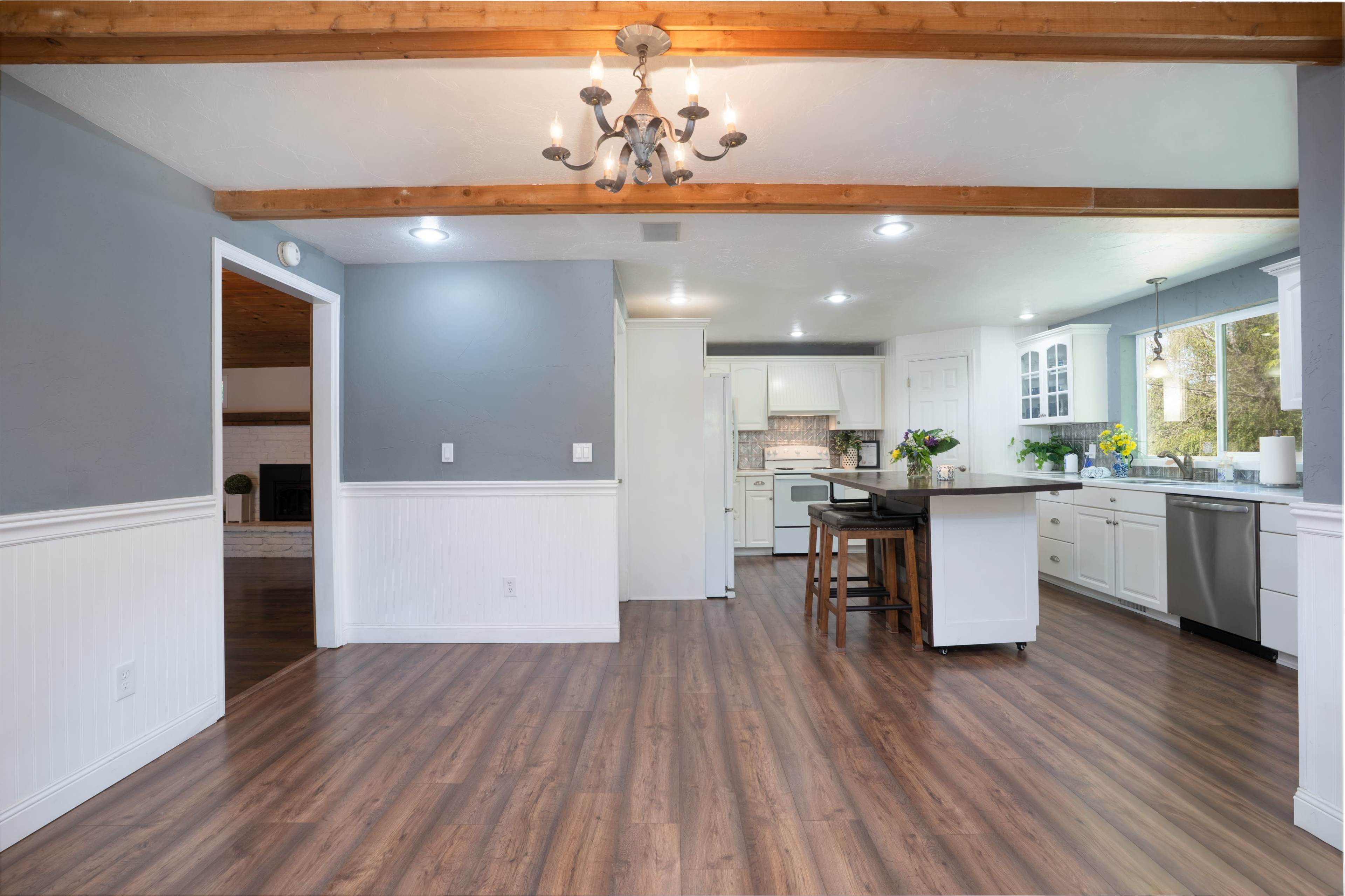 A modern kitchen and dining area features white cabinets, a central island with seating, and hardwood flooring, illuminated by a chandelier.