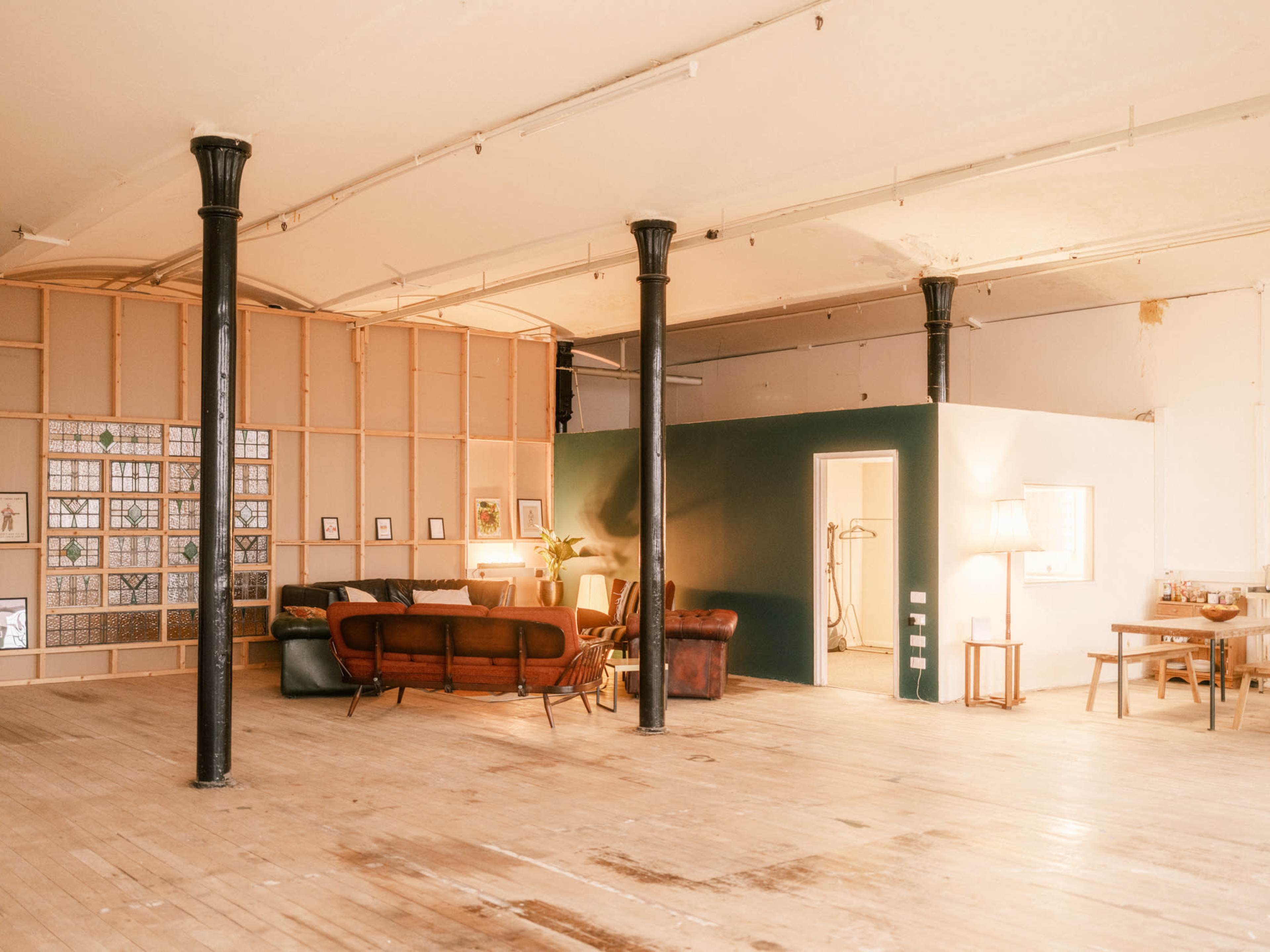 The image shows a spacious interior of a modern loft-style room with exposed beams, a seating area, and a dining space.