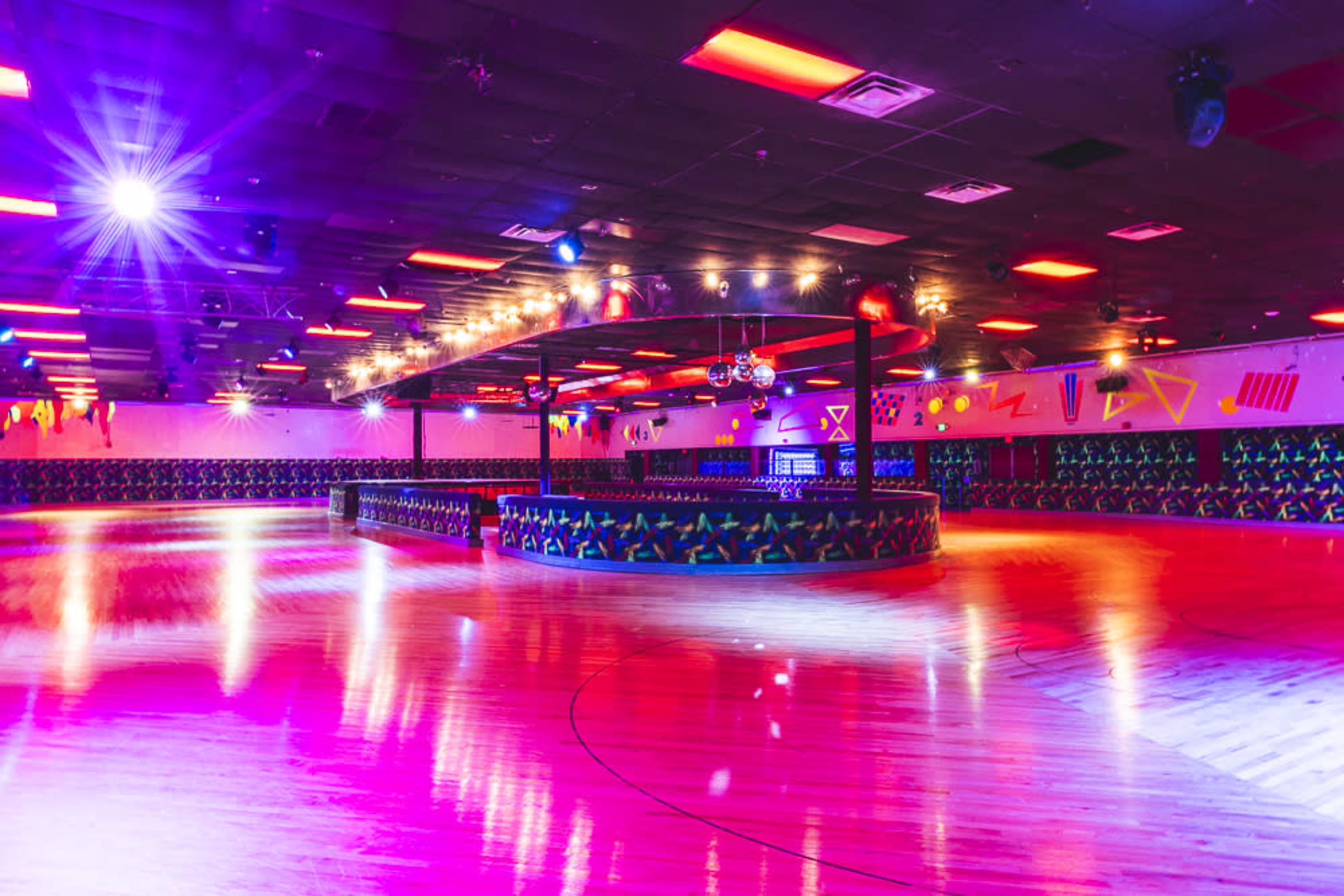 The image shows a vibrant roller skating rink with colorful lighting and a circular seating area.