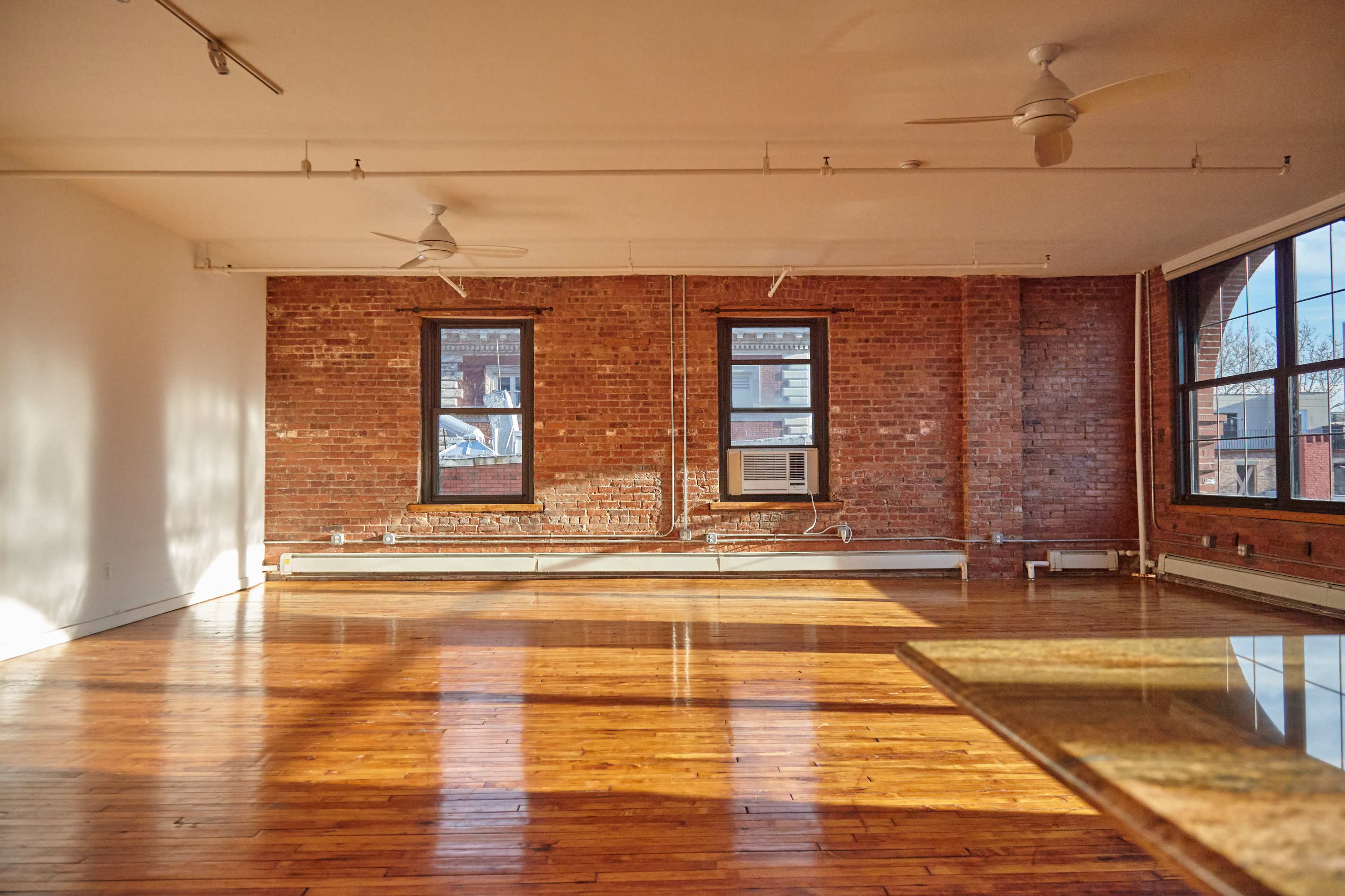 An empty room with exposed brick walls, large windows, and polished wooden floors.