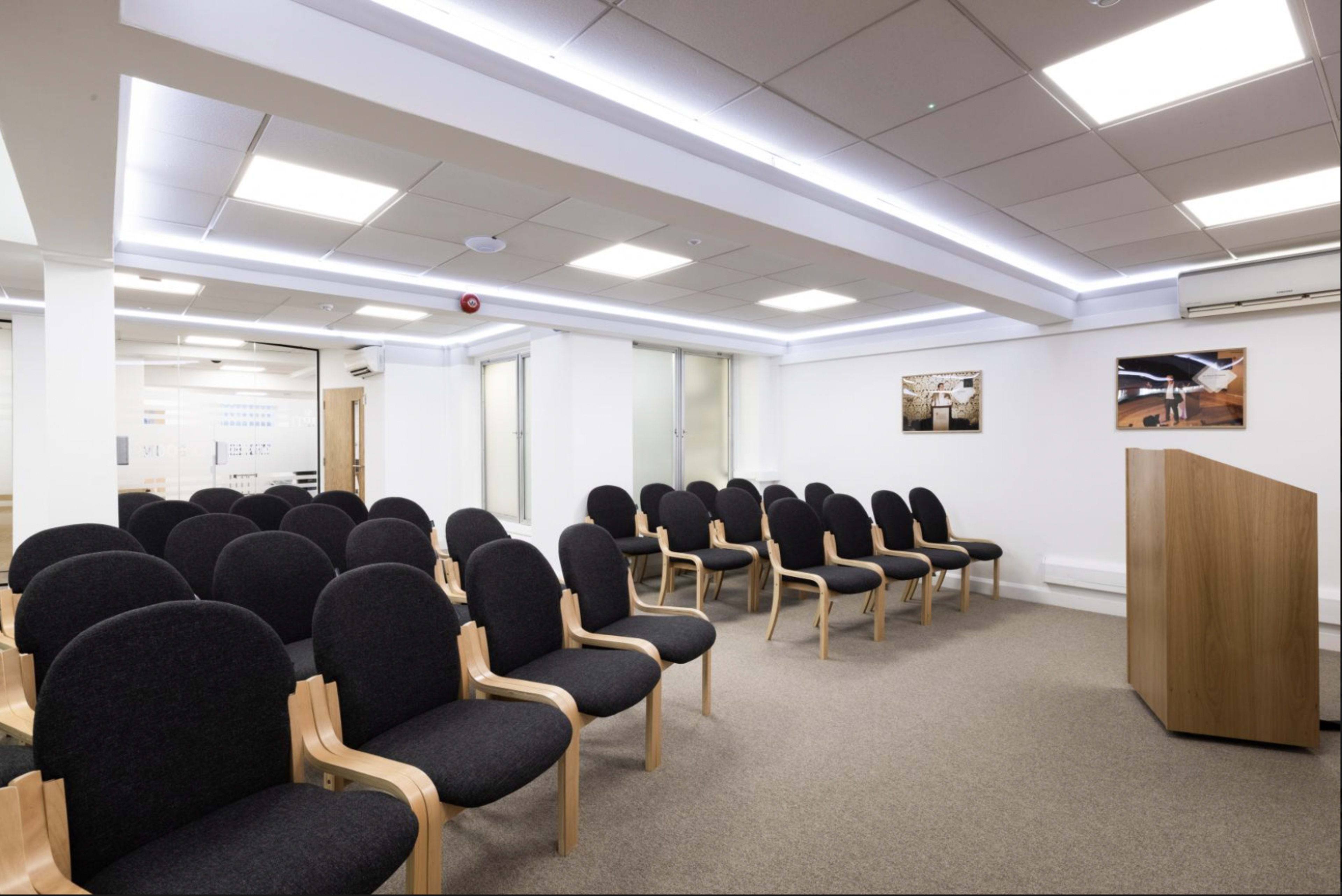 A modern conference room with rows of black upholstered chairs facing a wooden podium.