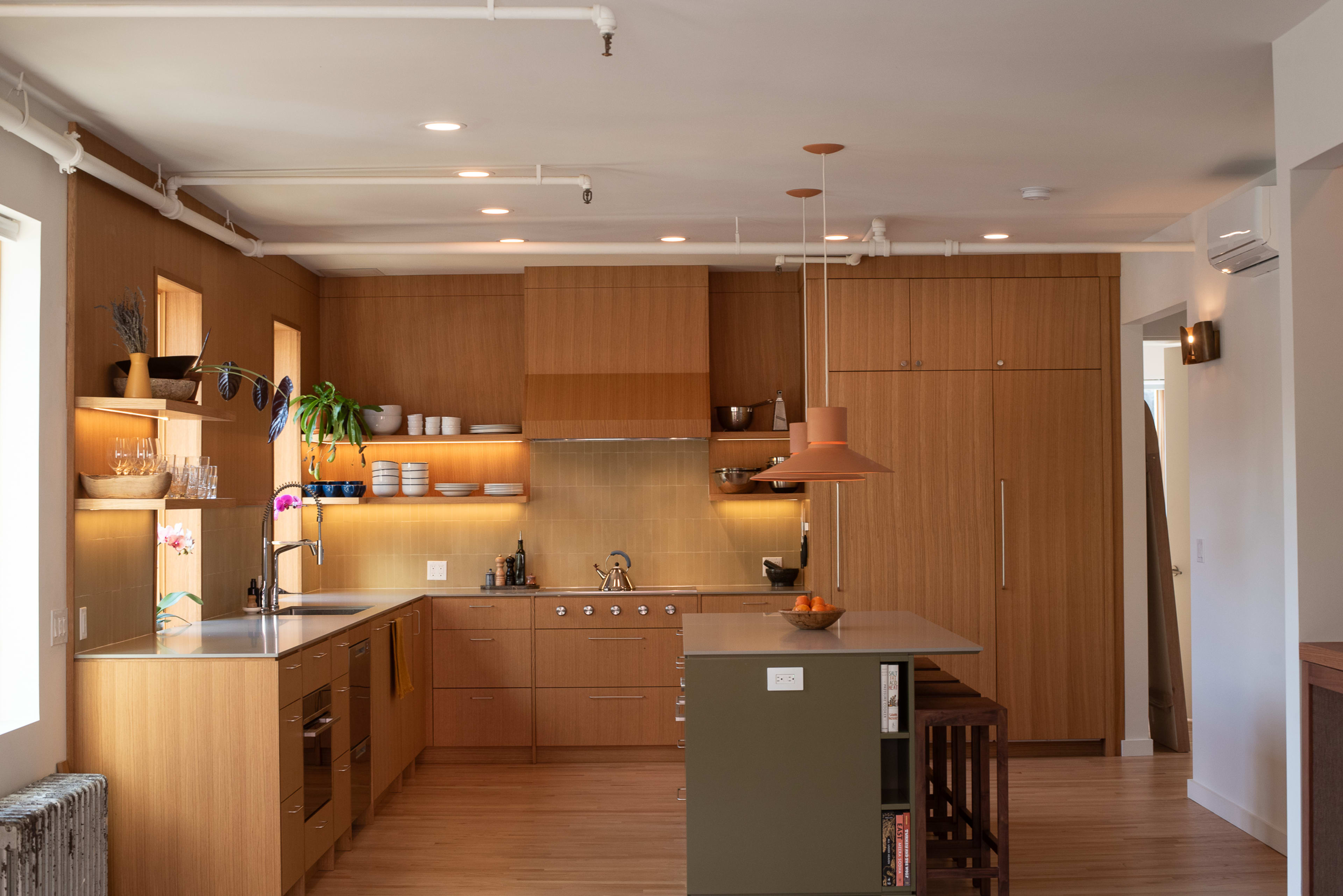 The image shows a modern kitchen with wooden cabinetry, a central island, and stainless steel appliances.