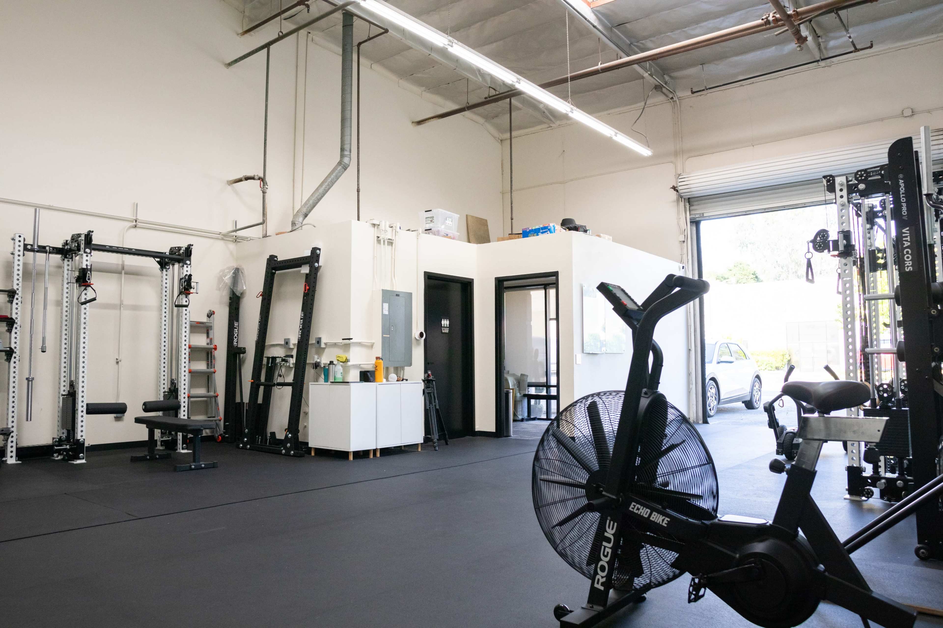 A modern gym interior with weightlifting equipment, a stationary bike, and a reception area.
