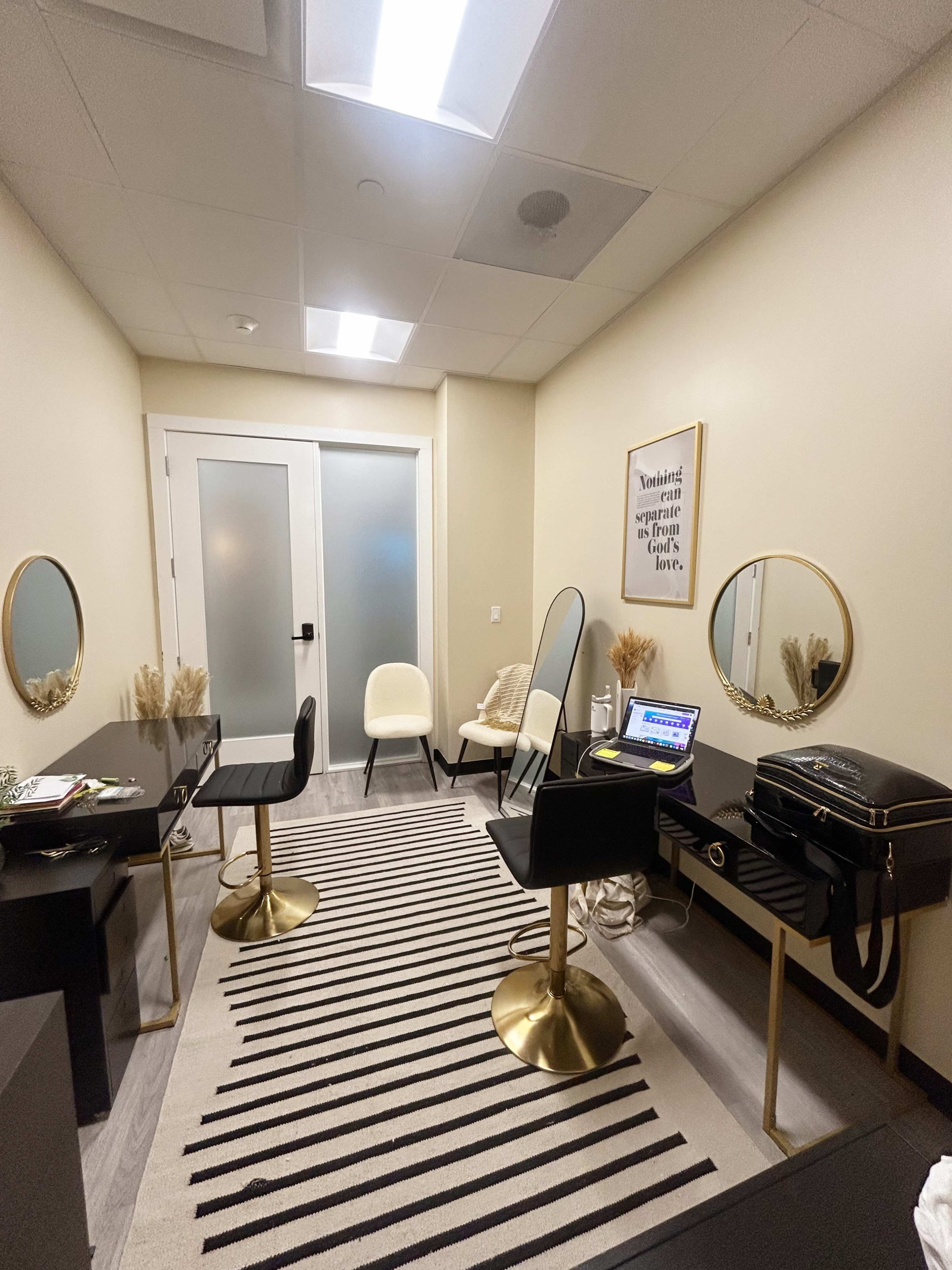 A modern, minimalistic office space with two black chairs, a desk with a laptop, a large mirror, and decorative elements on the floor and walls.