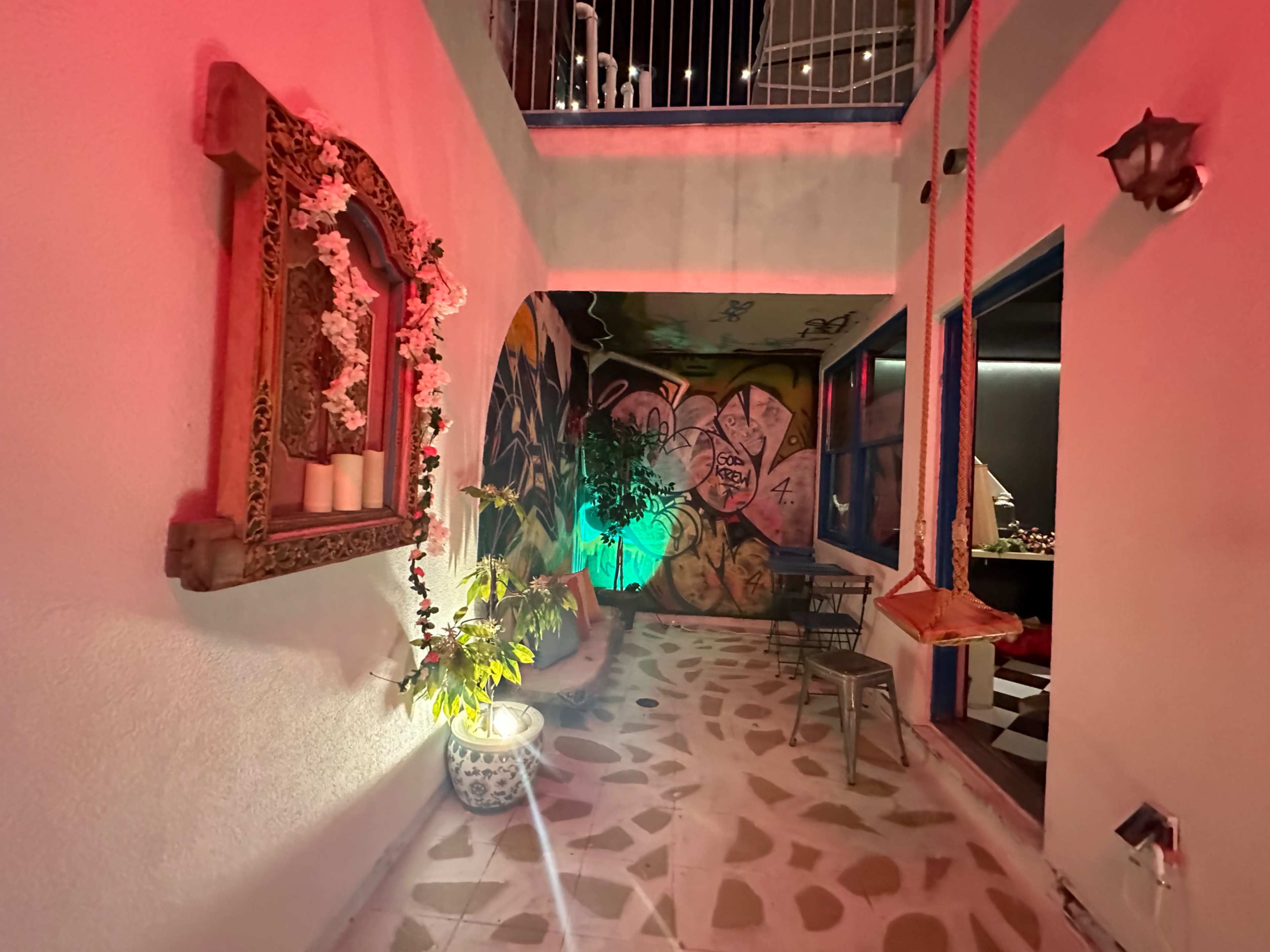 A hallway features a decorative mirror adorned with flowers, vibrant graffiti on the wall, and a swing hanging from the ceiling.