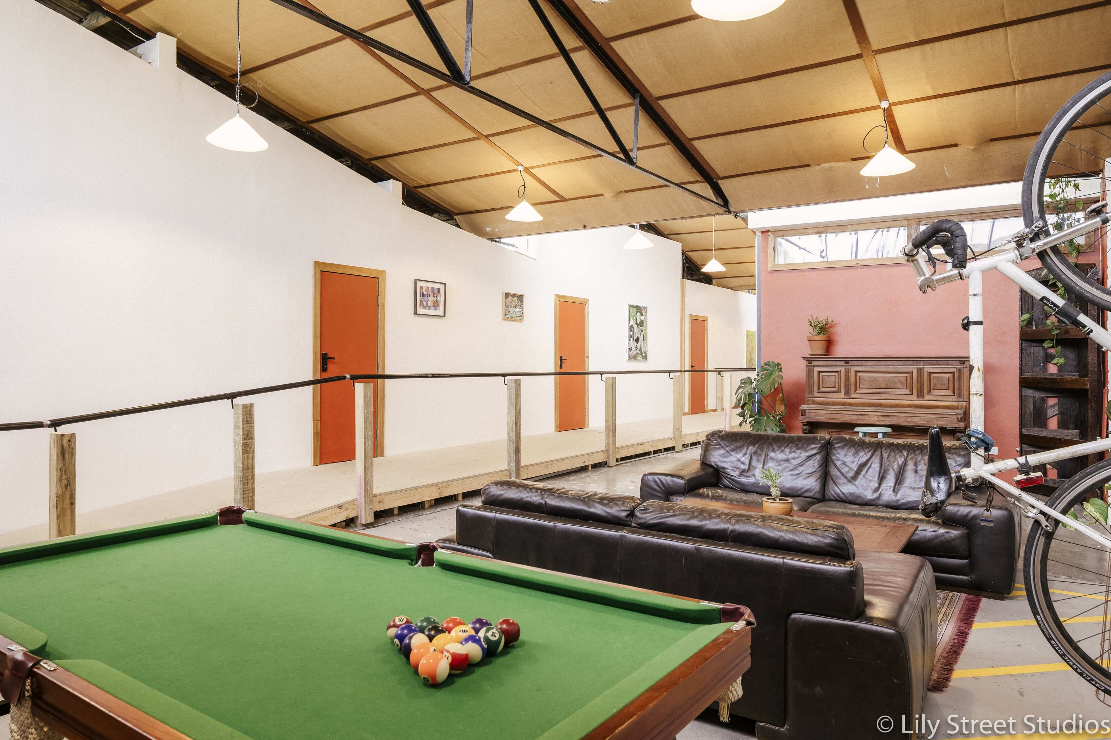 A recreational area with a green pool table, a black leather couch, and a hallway featuring several orange doors and artwork.